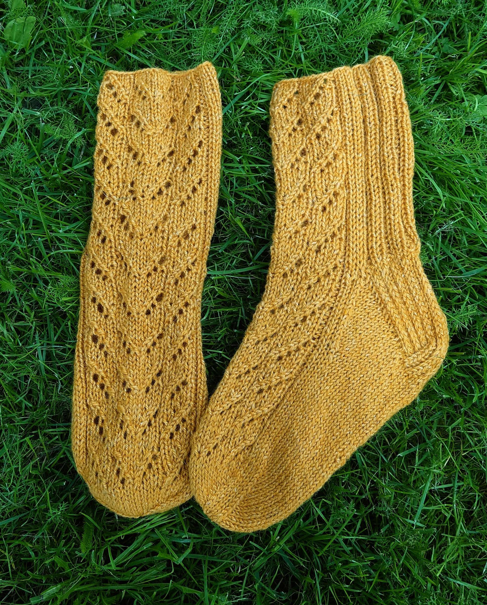 Hand knitted lace socks in color ochre. Shot on the grass. 
Käsin neulotut pitsisukat värissä okra. Kuvattu nurmikolla.