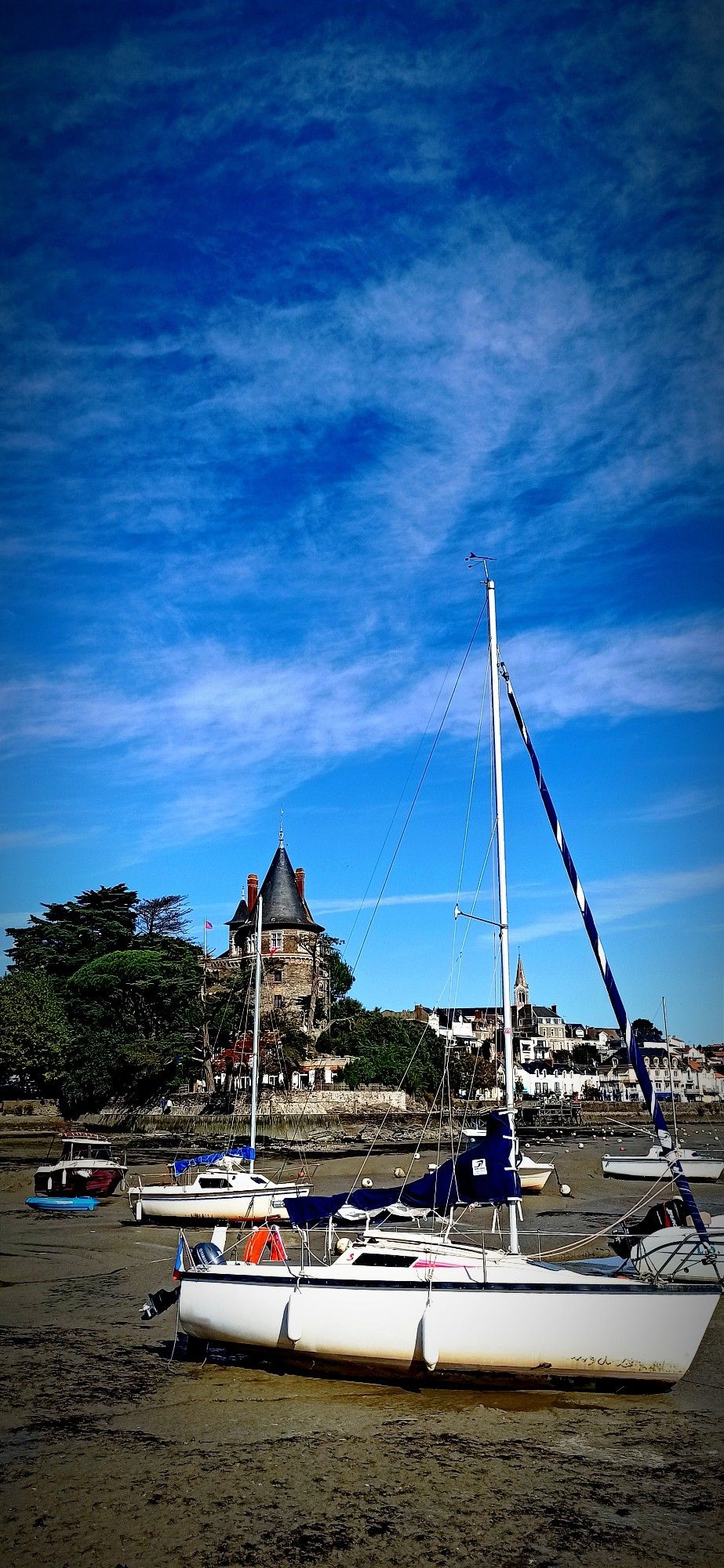 Port de Pornic à marée basse. Au loin on distingue les bâtiments et sur la gauche le château de la ville. Les bateaux sont posés sur la vase.