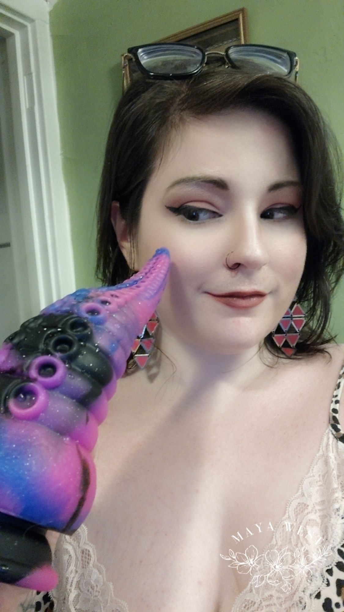 a brunette with her glasses pushed up on her head looks sidelong at a massive pink, blue and black tentacle dildo 