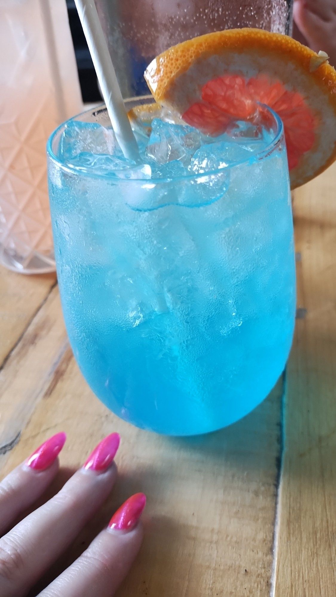 a sparkly blue drink in a round bottomed glass. there's a juicy half wheel of grapefruit as a garnish