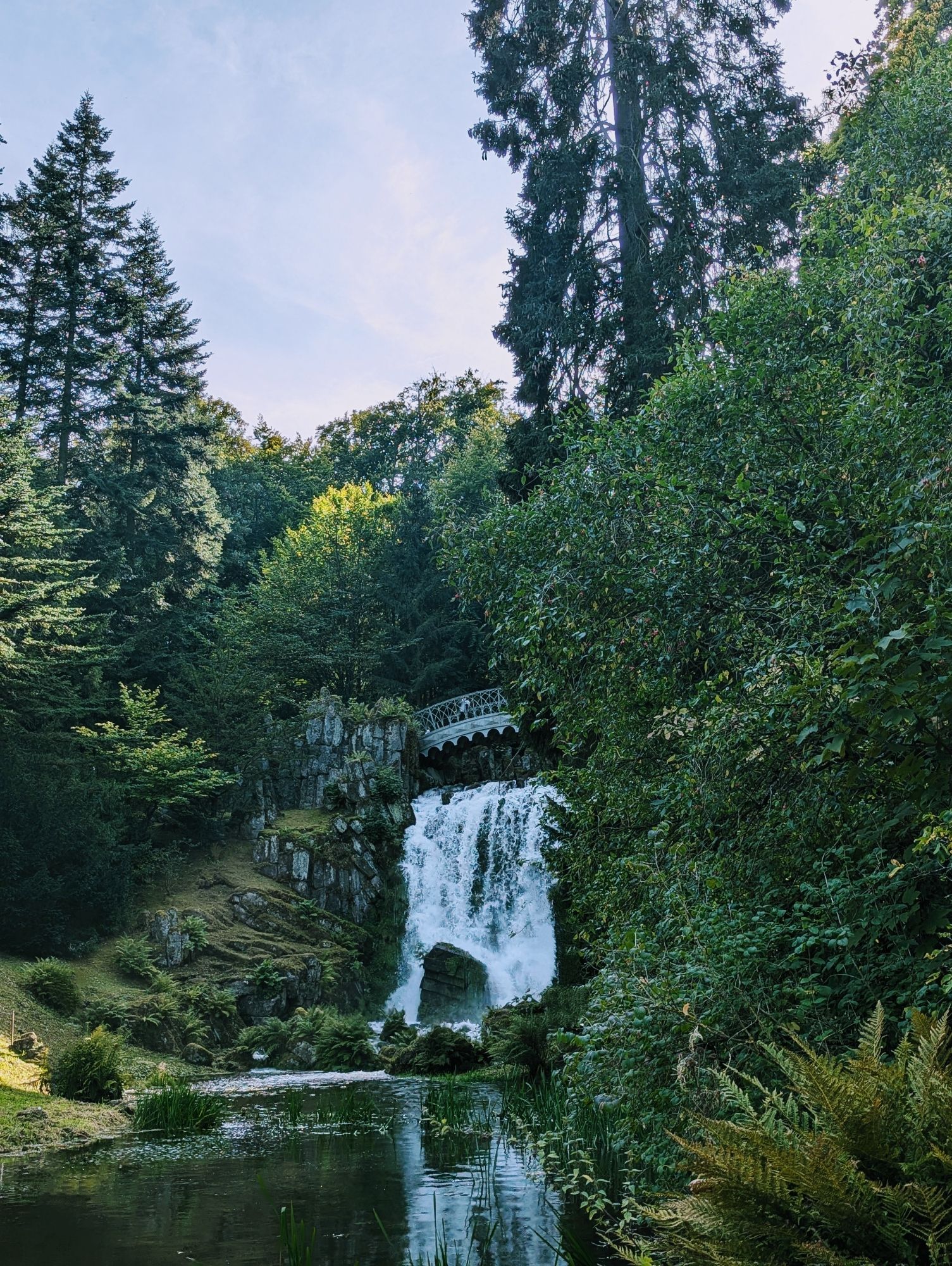 A photo of a man-made waterfall feature, surrounded by lush greenery and rocks.