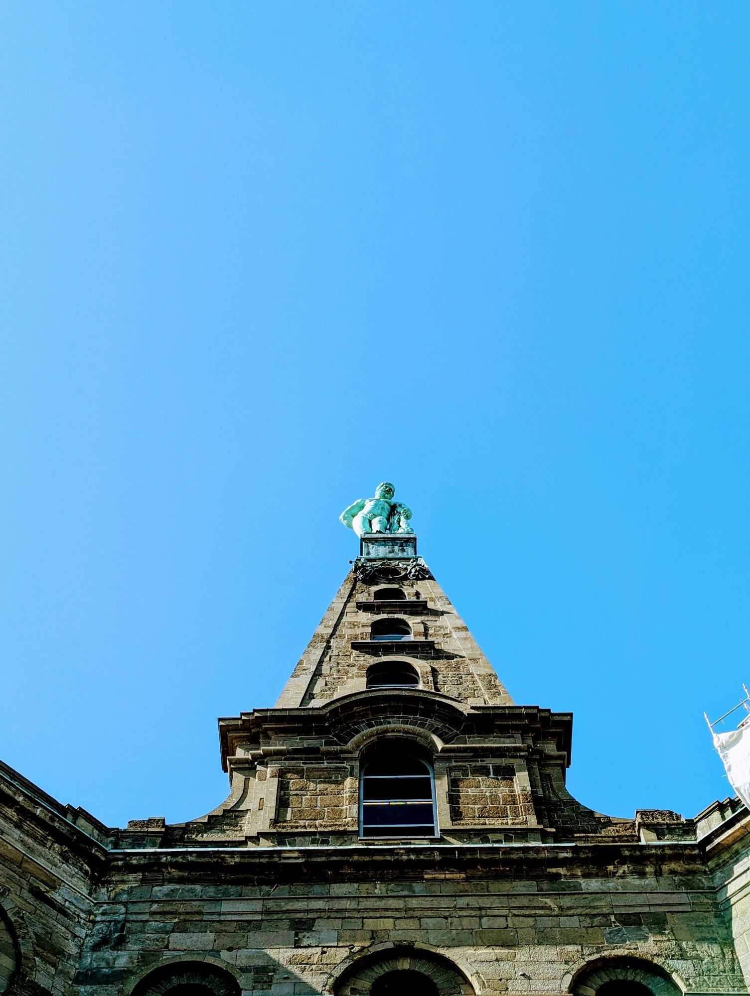 A picture taken from the ground, looking up at a tall monument with a bronze statue of Hercules at the very top.