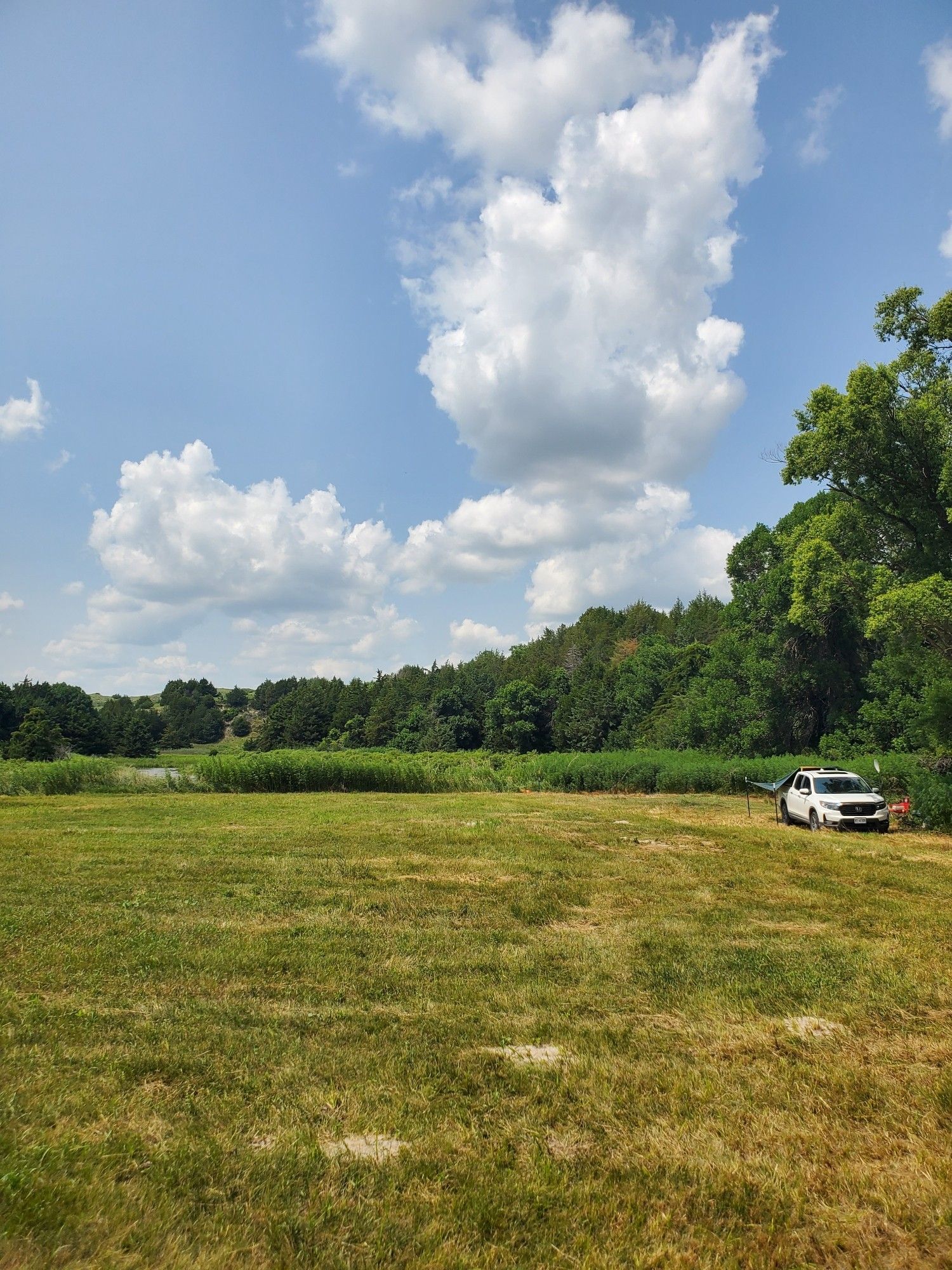 Mowed hayfield/meadow bordering a remote river surrounded by a partly cloudy blue sky and ringed with trees deep in the Nebraska Sandhills..