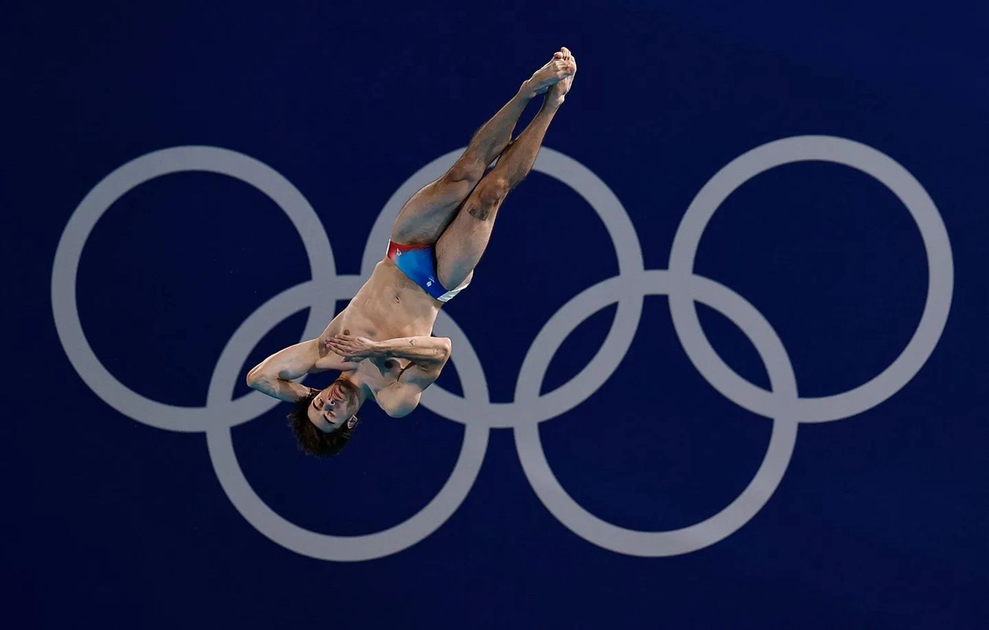 Le plongeur français Jules Bouyer en plein plongeon et, en fond, les anneaux olympiques