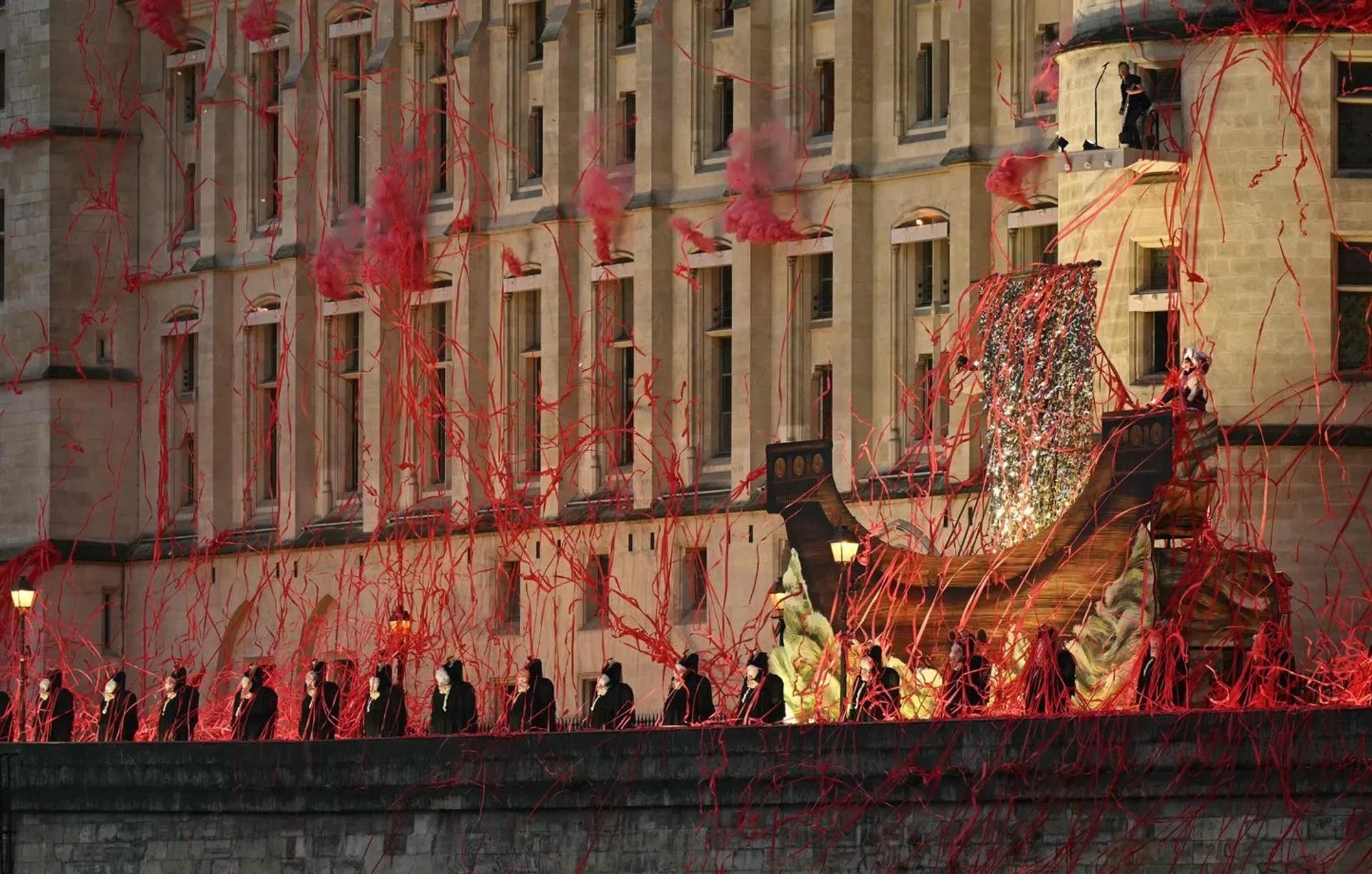 Des rubans rouges représentant du sang s’étalent depuis les fenêtres le long de la façade de la Conciergerie où le groupe Gojira a performé pendant la cérémonie d’ouverture des JO 2024. Devant le bâtiment passe un bateau représentant celui qui orne le blason de la ville de Paris