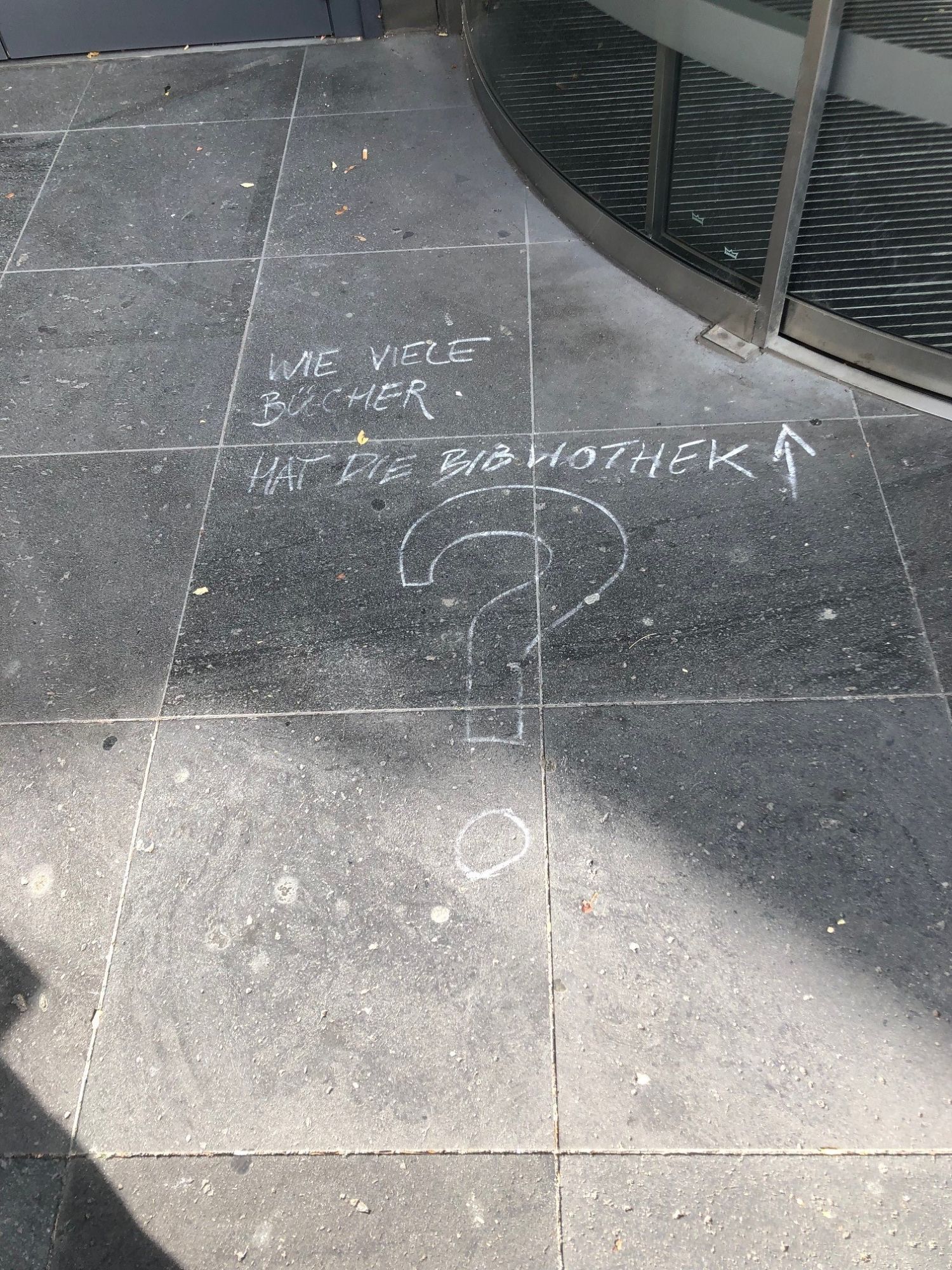 Kreideschriftzug "Wie viele Bücher hat die Bibliothek?" auf dem Boden vor der Teilbibliothek Geisteswissenschaften der ThULB Jena.