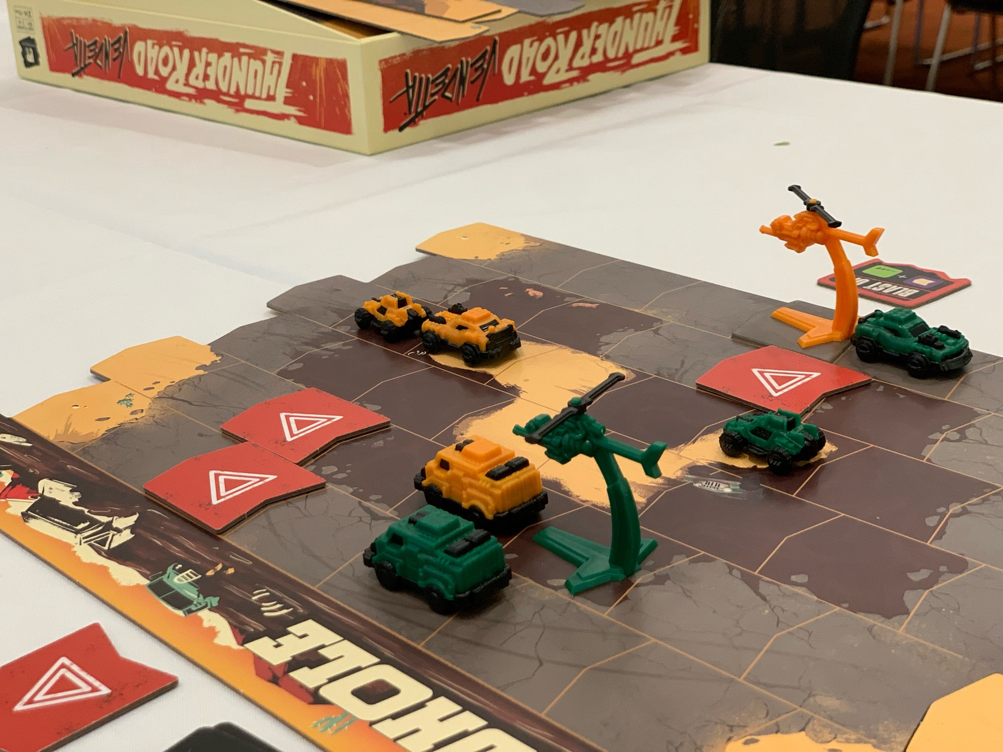 Orange and green cars and copters racing down a wasteland board