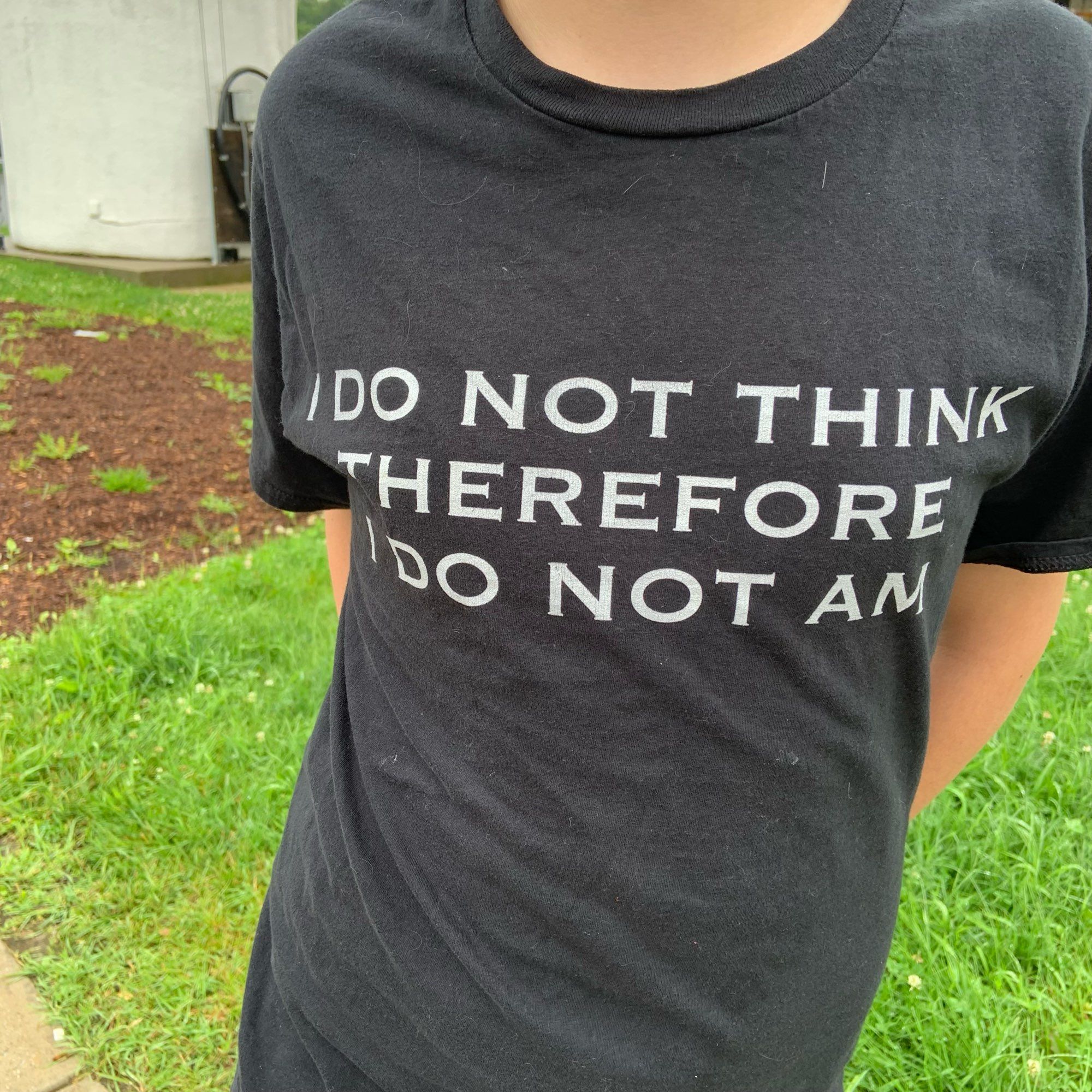 Kid’s torso in a dark gray t shirt reading “I DO NOT THINK THEREFORE I DO NOT AM”