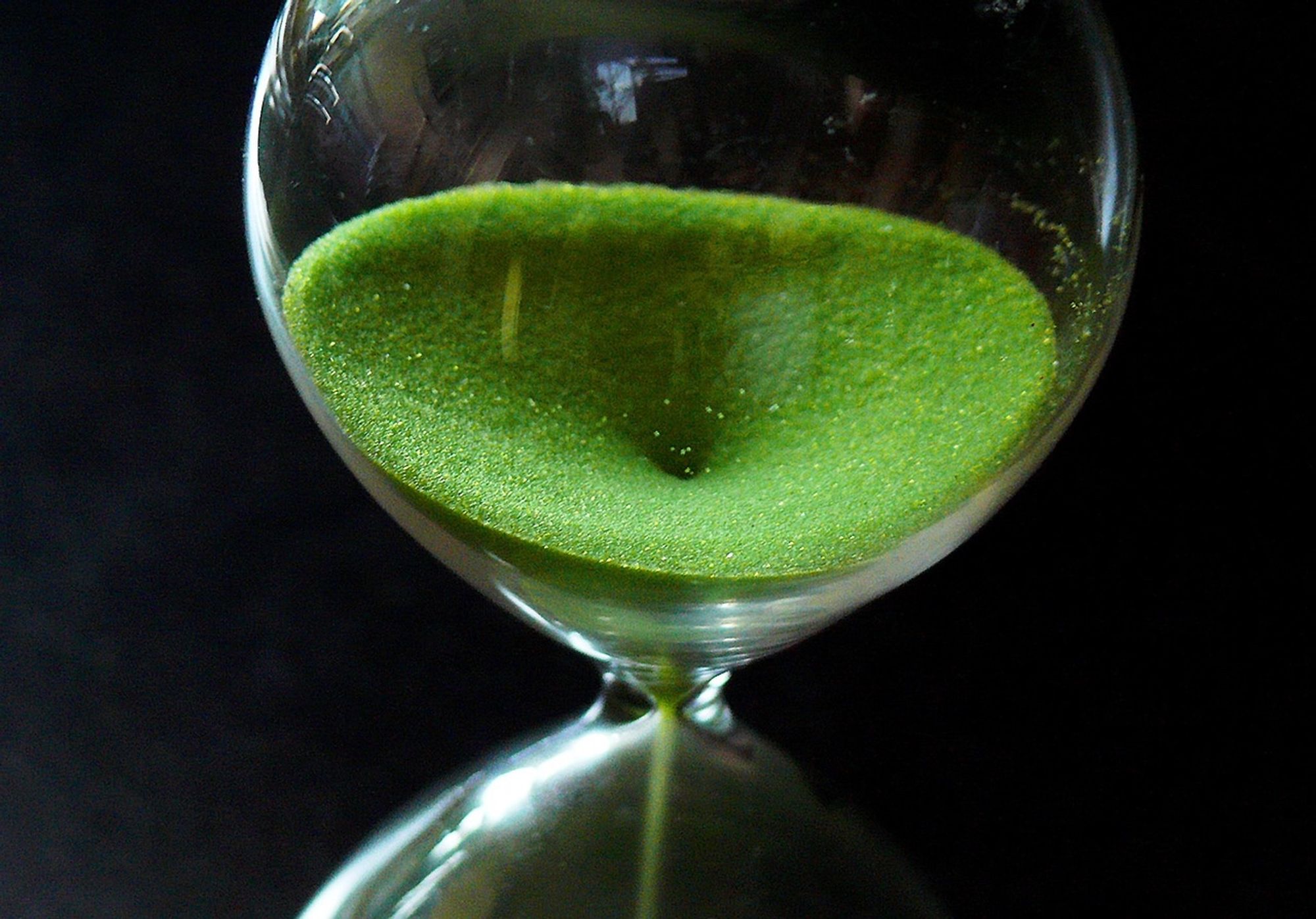 picture of glass hourglass with green sand almost empty