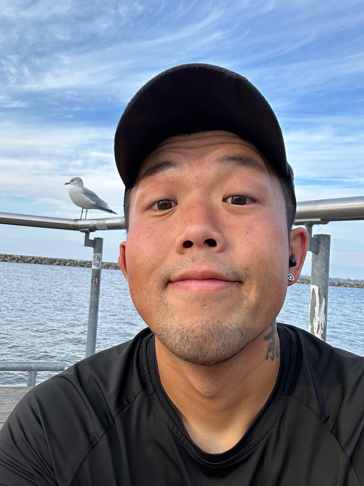 Me in sweaty running shirt and cap, sitting on the dock with a seagull in the background as the sun rises in the east.