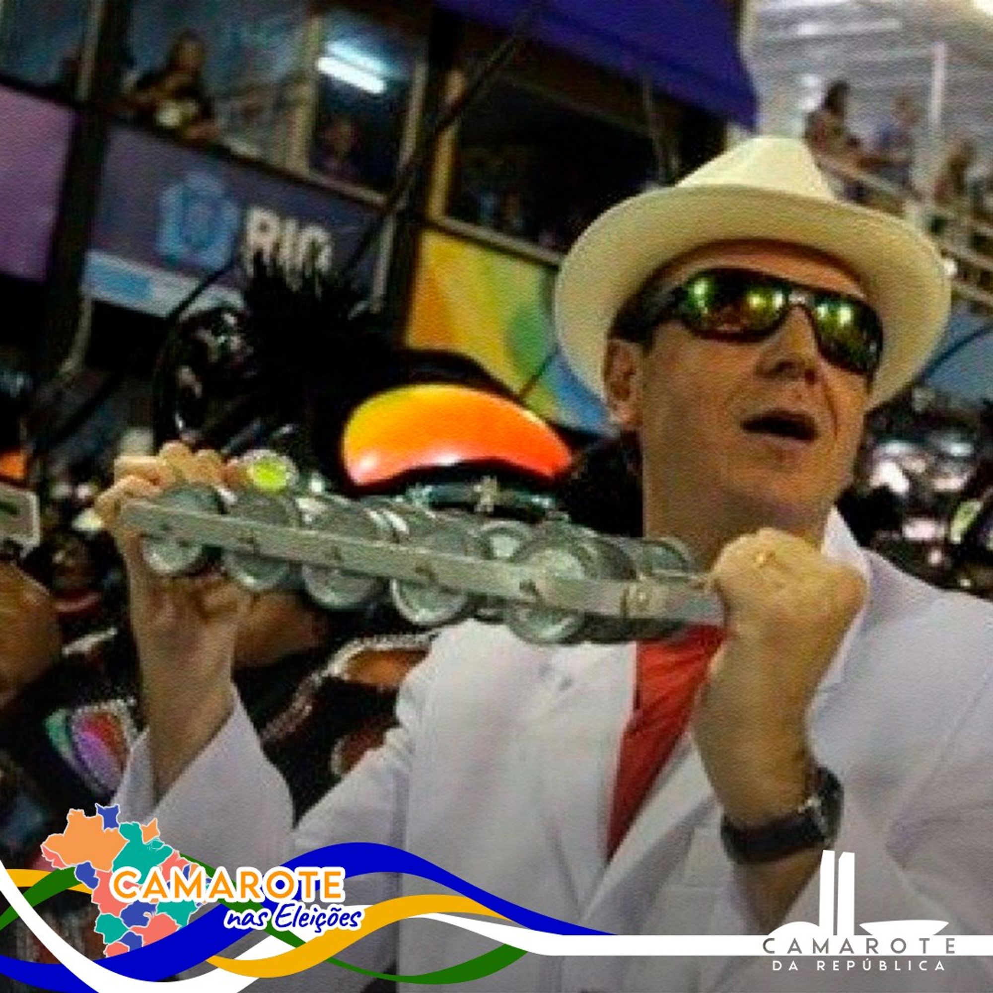 Eduardo Paes, prefeito do Rio de Janeiro, aparece em um ambiente festivo, vestindo um terno branco e um chapéu estilo panamá. Ele está segurando um instrumento musical (um ganzá) e usando óculos escuros, provavelmente durante um desfile de carnaval. O fundo indica uma arquibancada lotada e luzes brilhantes. Os logos "Camarote nas Eleições" e "Camarote da República" também aparecem nos cantos inferiores da imagem.