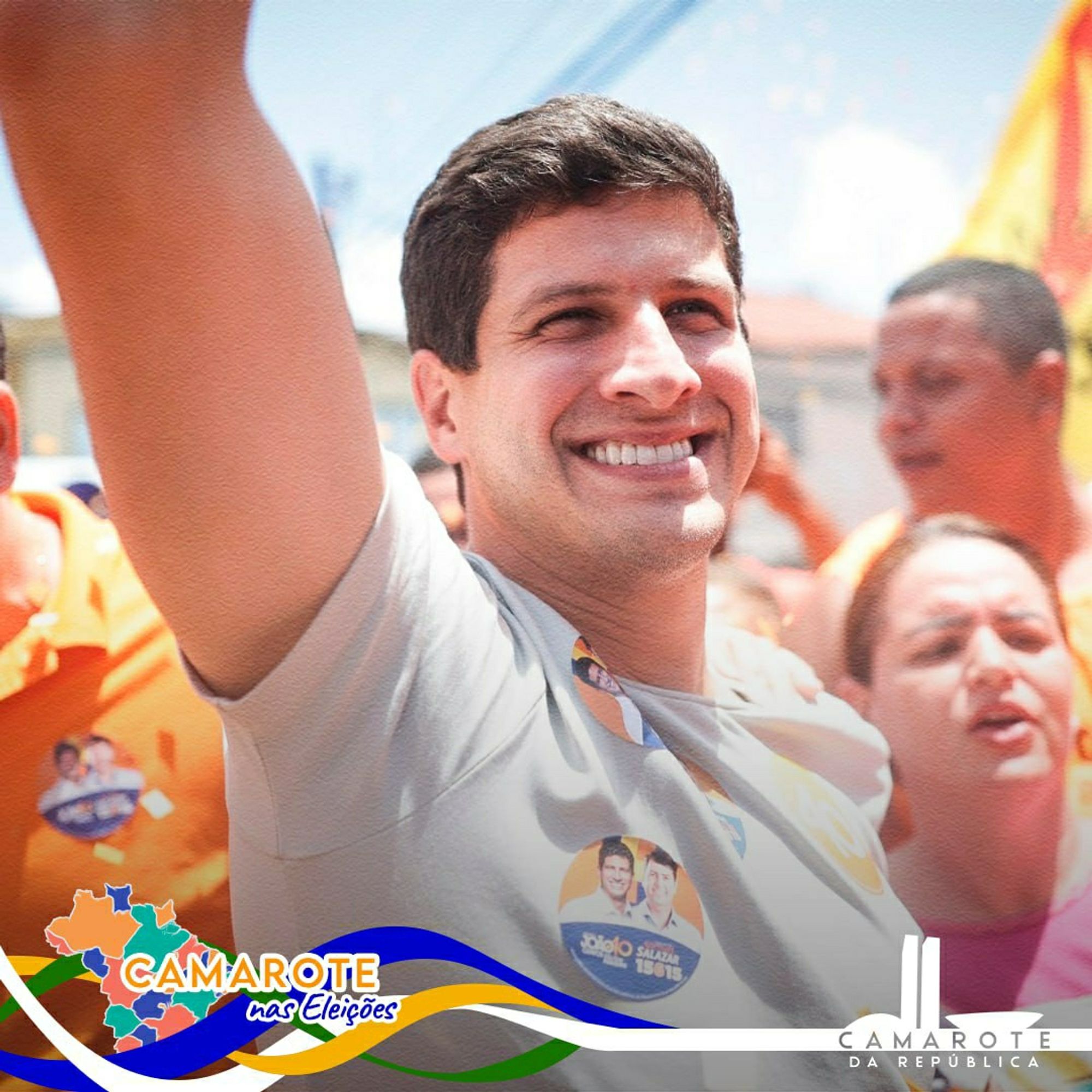 Imagem de João Campos, prefeito do Recife e candidato à reeleição, durante um evento de campanha. Ele está sorrindo e acenando com o braço direito levantado, cercado por apoiadores. Usa uma camisa clara com adesivos de campanha presos no peito, mostrando sua foto ao lado de seu número de candidatura. Ao fundo, algumas pessoas vestem roupas de campanha em tons de laranja e carregam bandeiras. O céu está claro, sugerindo um dia ensolarado. No canto inferior esquerdo, aparece o logo colorido do "Camarote nas Eleições" e no canto inferior direito, o logo do "Camarote da República".