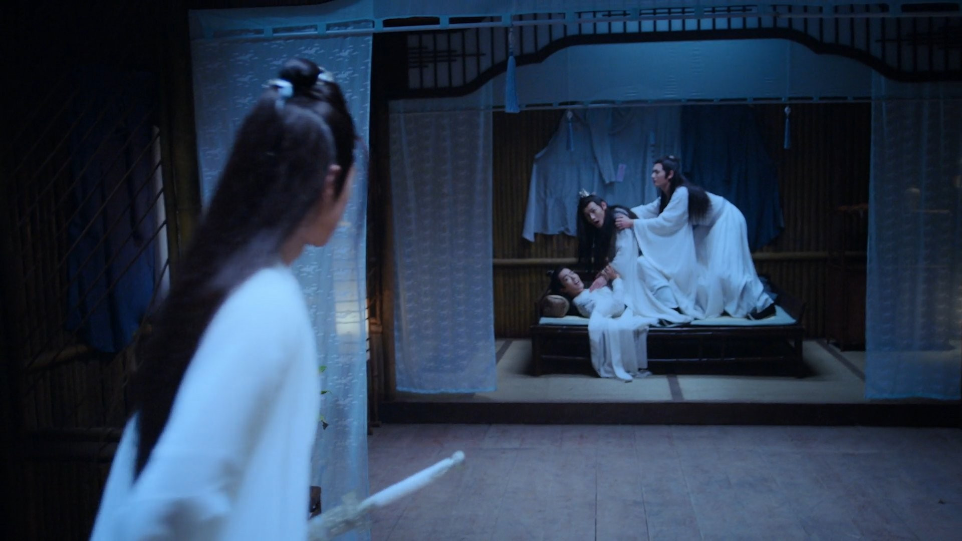 Teen Lan Wangji enters a guest dormitory room while on patrol to find three guests disciples - Wei Wuxian, Jiang Cheng, and Nie Huaisang - in an interesting configuration. All three are on the bed opposite the offscreen door through which Wangji entered, Wuxian flat in his back at the bottom of the pile, Jiang Cheng crouched over him and gripping the front of his robes in sibling frustration, and Huaisang behind Jiang Cheng gripping his shoulders in an attempt to pull him back. Frozen in tableau, it appears quite compromising. Wuxian and Jiang Cheng have turned their heads toward the entering Wangji.