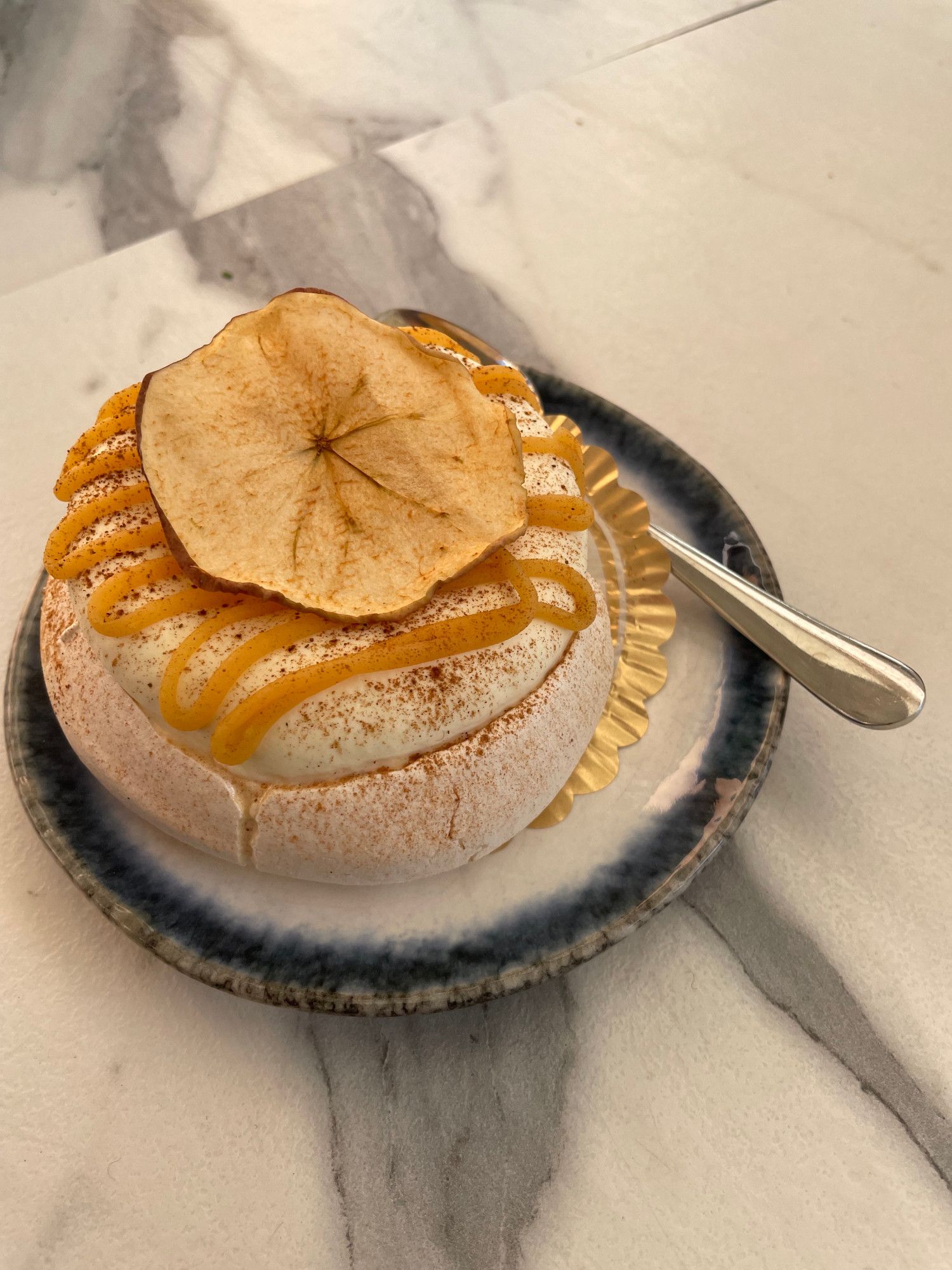 A mini pavlova topped with caramel drizzle, cinnamon, and dried apple. Apple compote is hidden inside the pavlova.