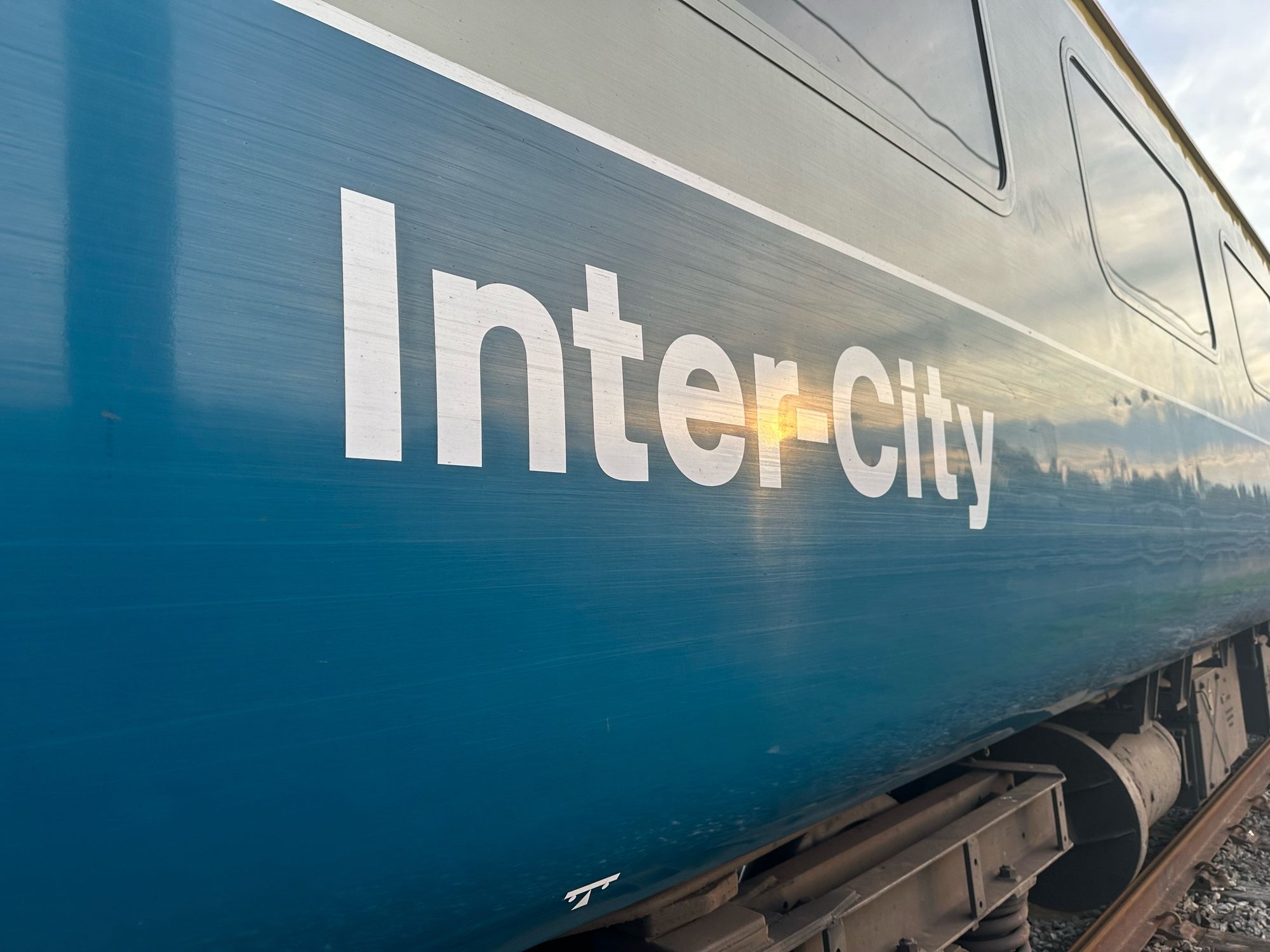 A sunset is reflected in the white Inter-City text of a 1970s grey and blue mark 2 passenger coach that used to work on the railways of Great Britain.