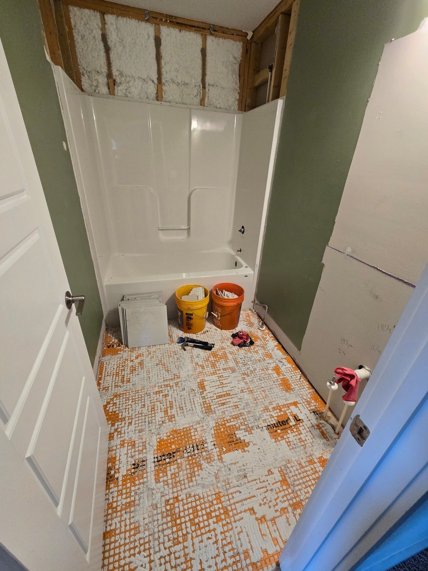 A bathroom with no tile on the floor, some squares of tile are stacked against the tub and others are broken in two 5 gallon buckets. On the floor is remains of mortar and orange waterproofing which also needs to come up, but that's a tomorrow problem.