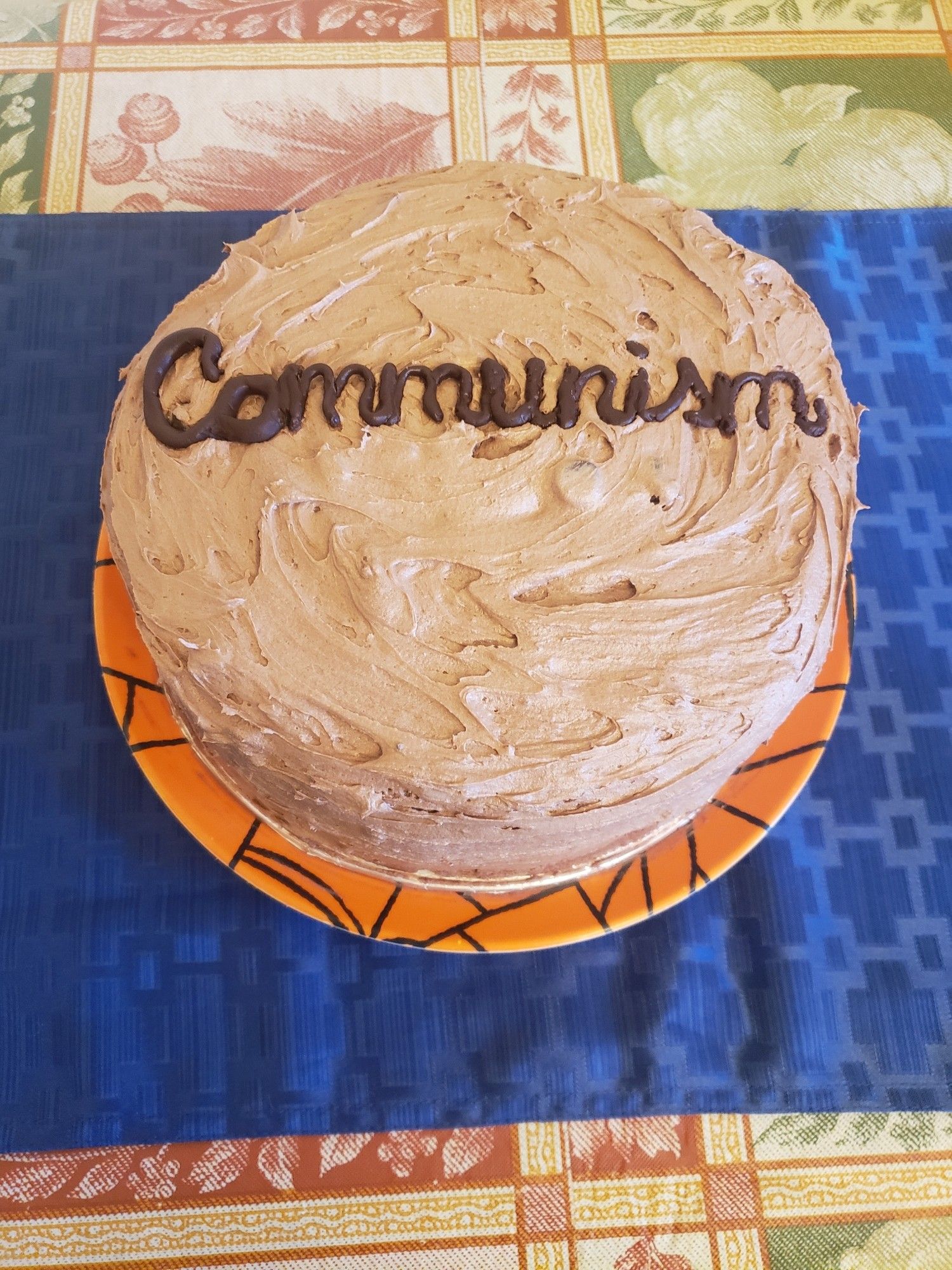 Chocolate cake that reads "communisim" on an orange spider-web plate