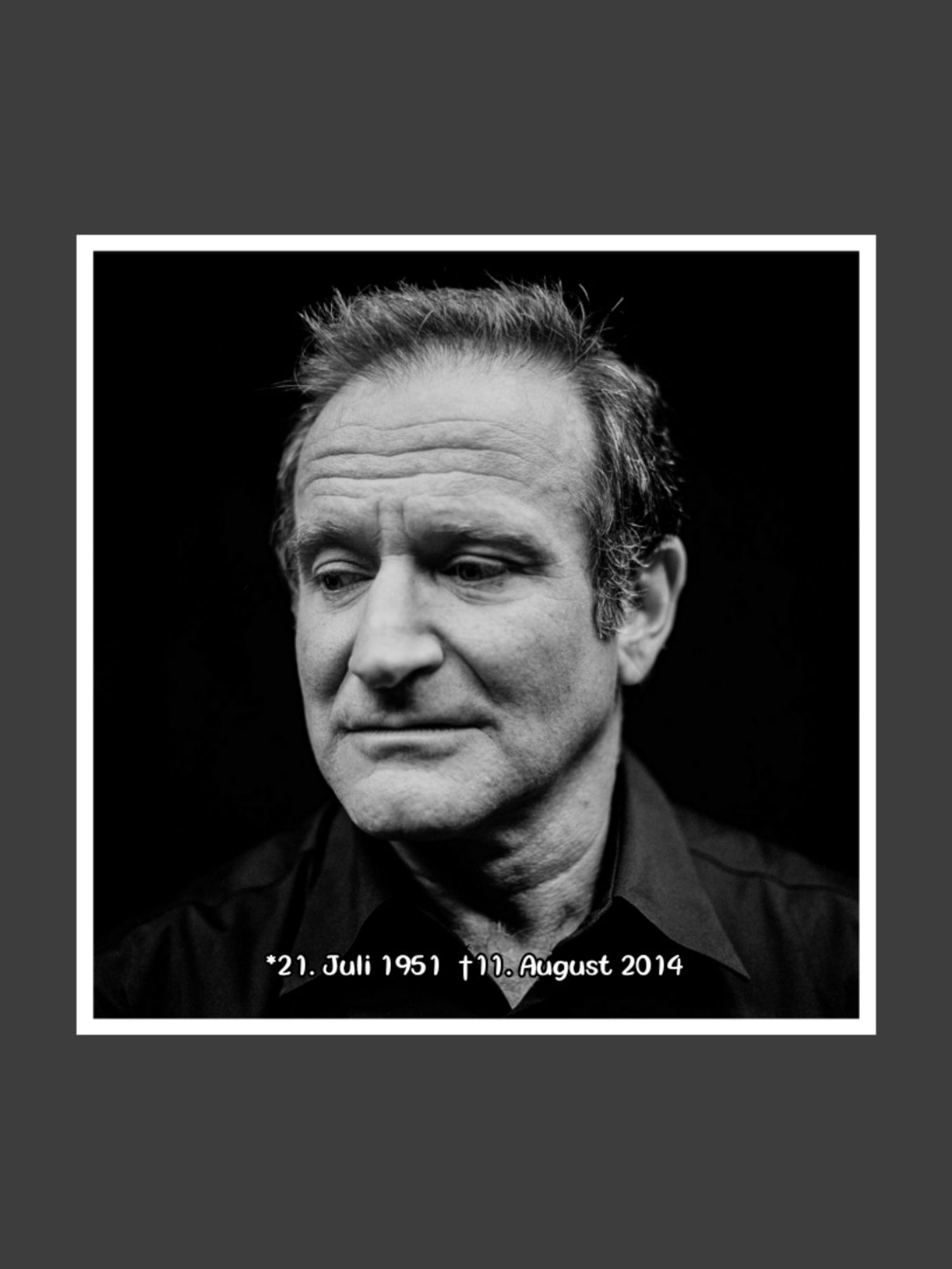 Schwarz-Weiß Foto vom Schauspieler Robin Williams. Er guckt nachdenklich nach unten. Im Bild stehen sein Geburtstag (21.07.1951) und sein Todestag (11.08.2014). Ein dicker grauer Rahmen umschließt das Bild.