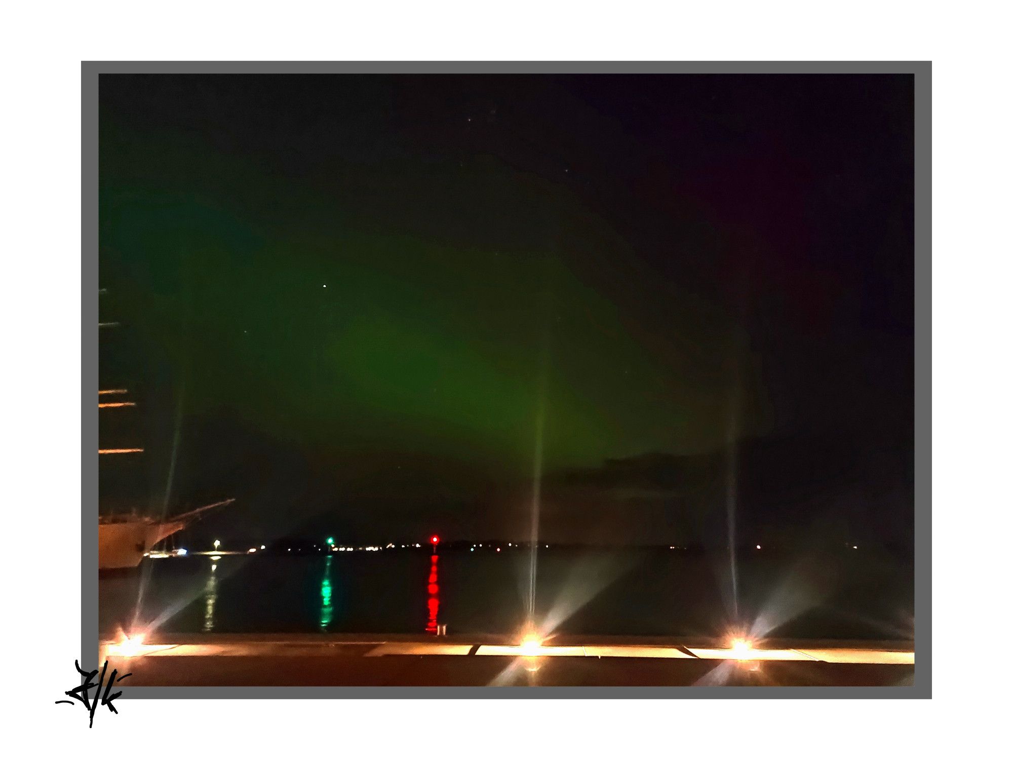 Foto vom nächtlichen Himmel über Rügen. Wieder der leuchtende grüne Streifen und in der Ferne zwei Fahrwassertonnen die mit grünem Licht Steuerbord und mit rotem Licht Backbord anzeigen. Vorn im Bild leuchten die Lichter der Stralsunder Hafenbeleuchtung und der Bug der Gorch Fock I ist an der linken Seite mit im Bild.