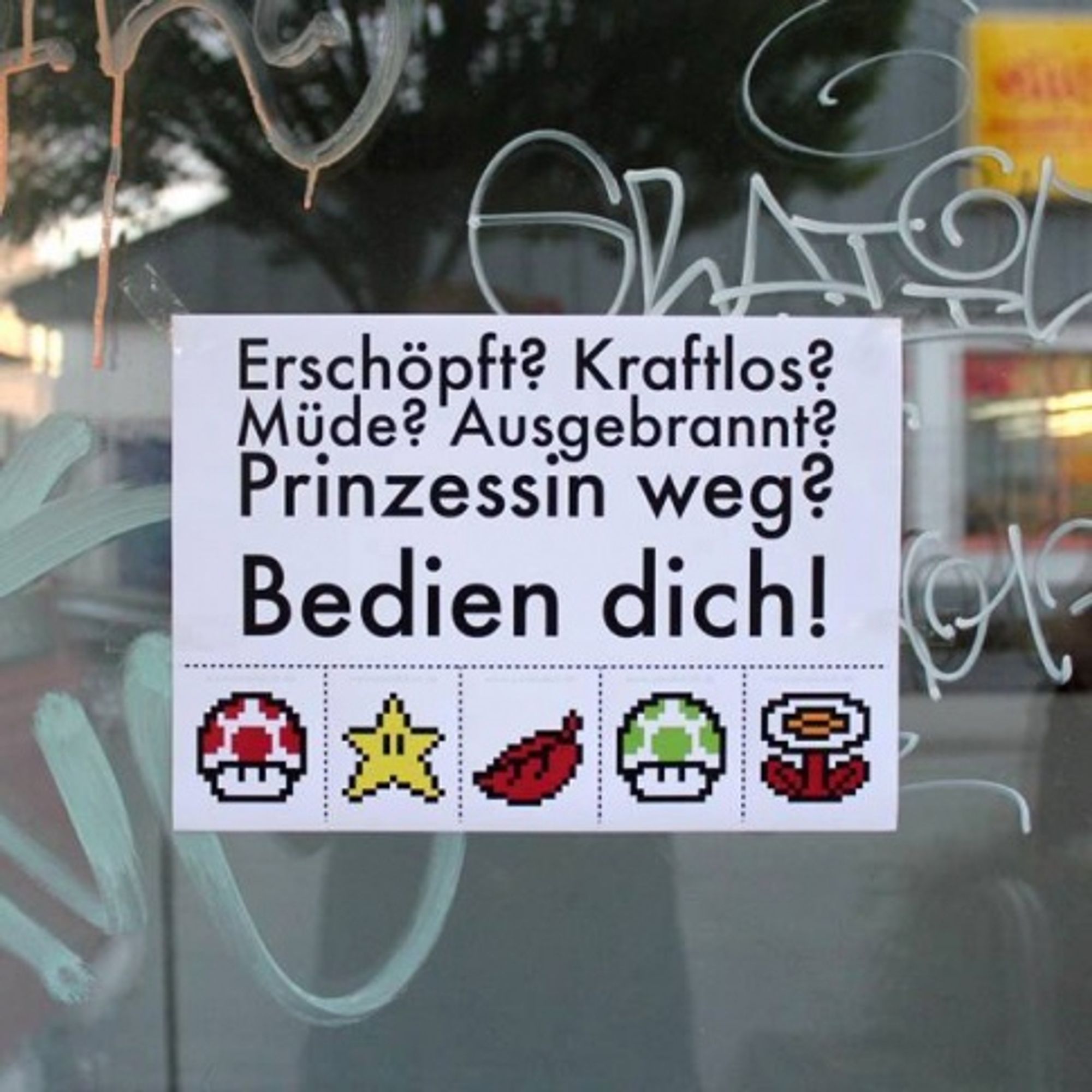 Ein Zettel an einer Glasscheibe mit dem Text: "Erschöpft? Kraftlos? Müde? Ausgebrannt? Prinzessin weg? Bedien dich!"
Darunter Abreißzettel mit Super Mario Symbole. (Roter Pilz, Stern, Blatt, Grüner Pilz, Blume)