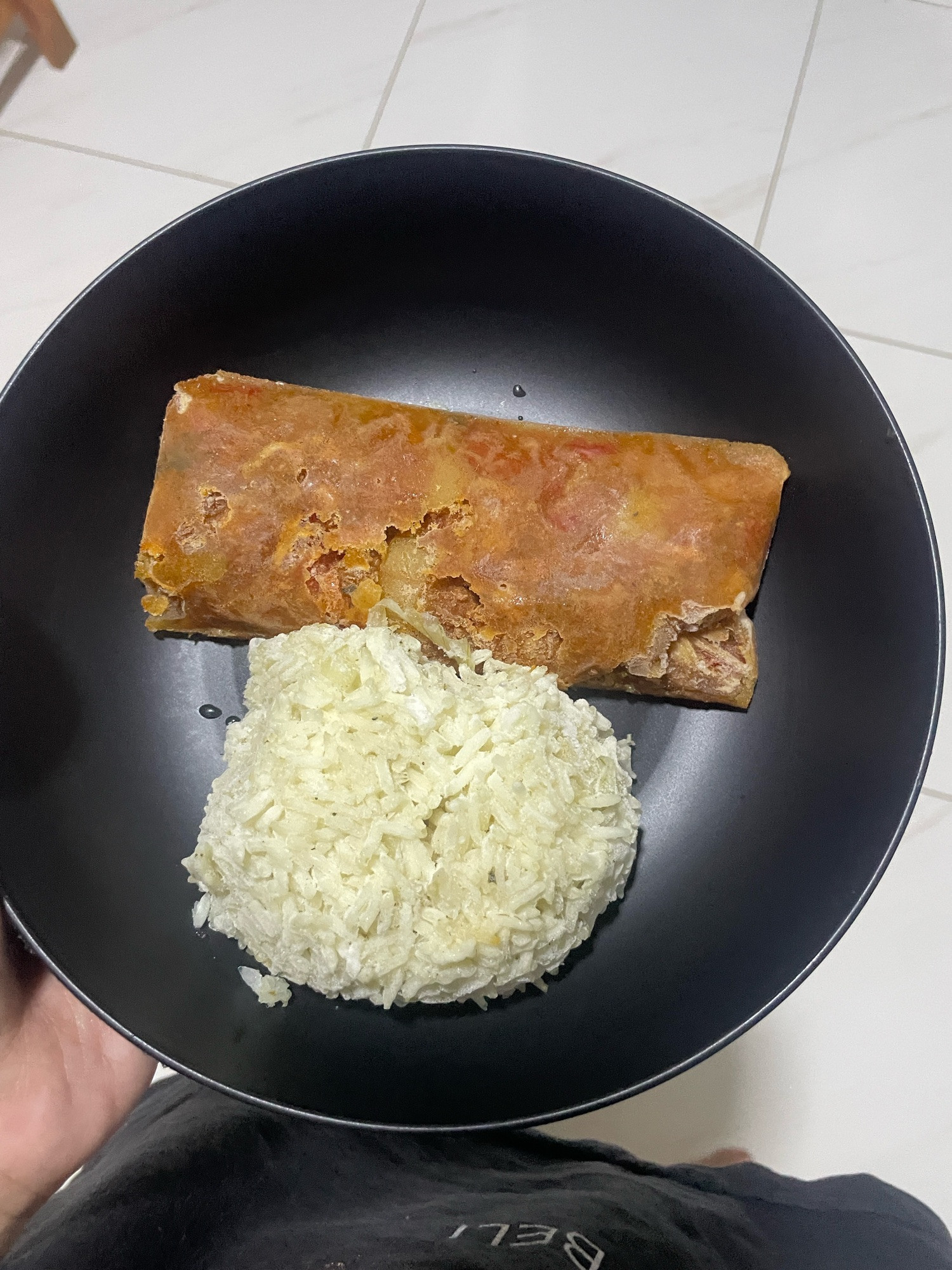 um prato preto onde está disposto um curry congelado em forma de retângulo laranja e uma bola de arroz branco