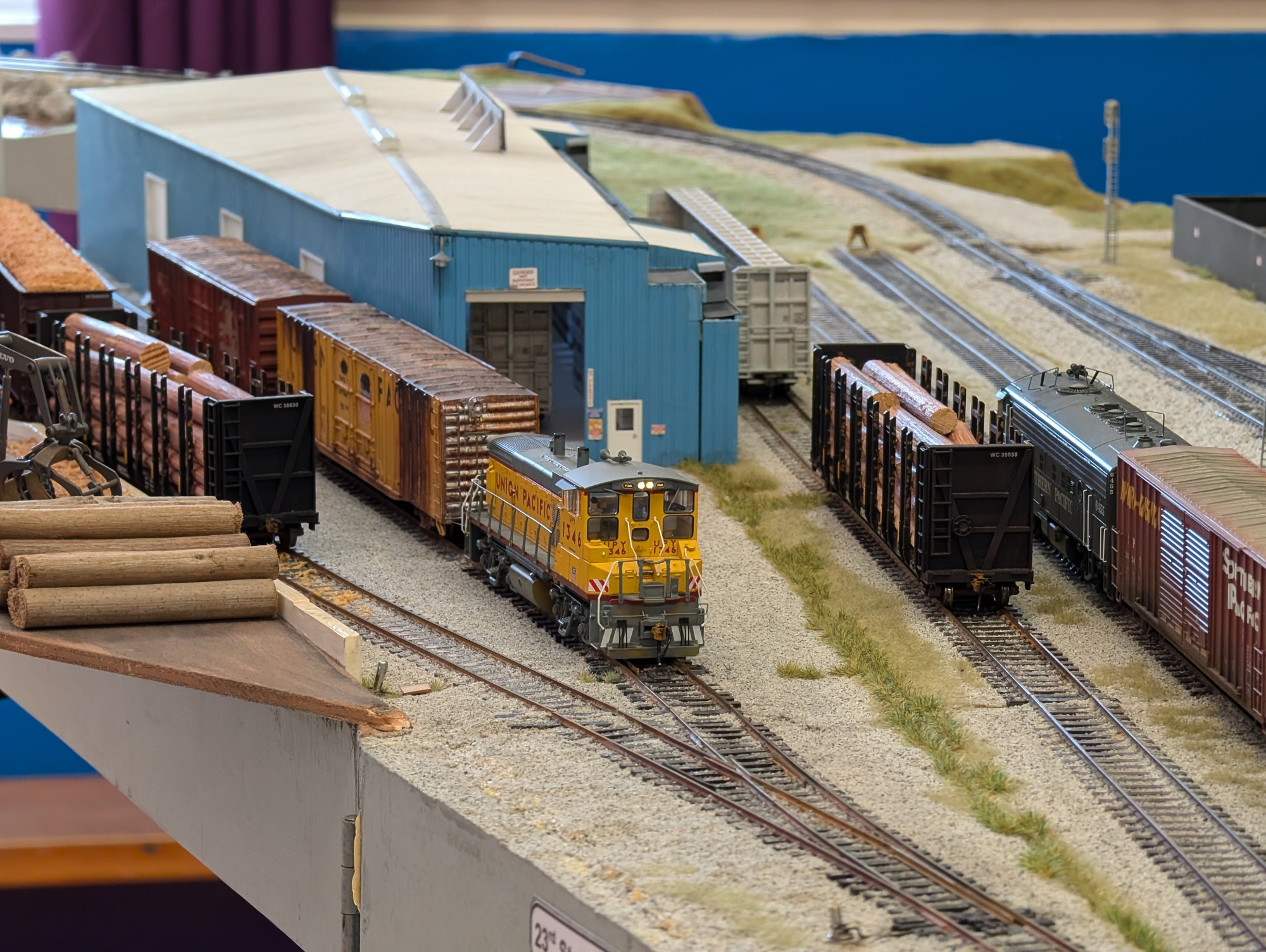 A yellow and grey diesel shunting freightcars at a blue warehouse 