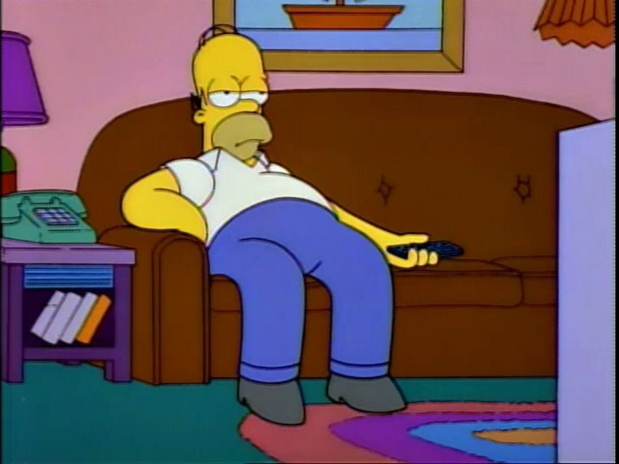 Homer Simpson sitzt gelangweilt auf einem braunen Sofa, hält eine Fernbedienung in der Hand und schaut zur Seite. Im Hintergrund steht ein grünes Telefon auf einem Tisch.