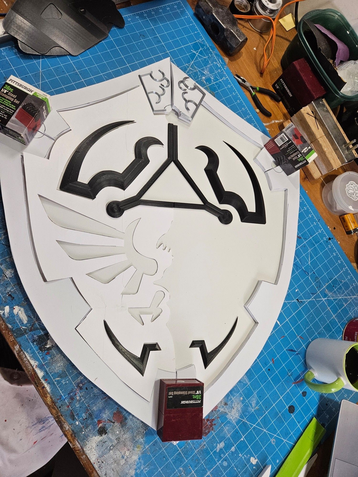 Work in progress eva foam replica hylian shield from legend of zelda twilight princess.  Template and 3d printed devices are arranged on its surface, held in place by weights