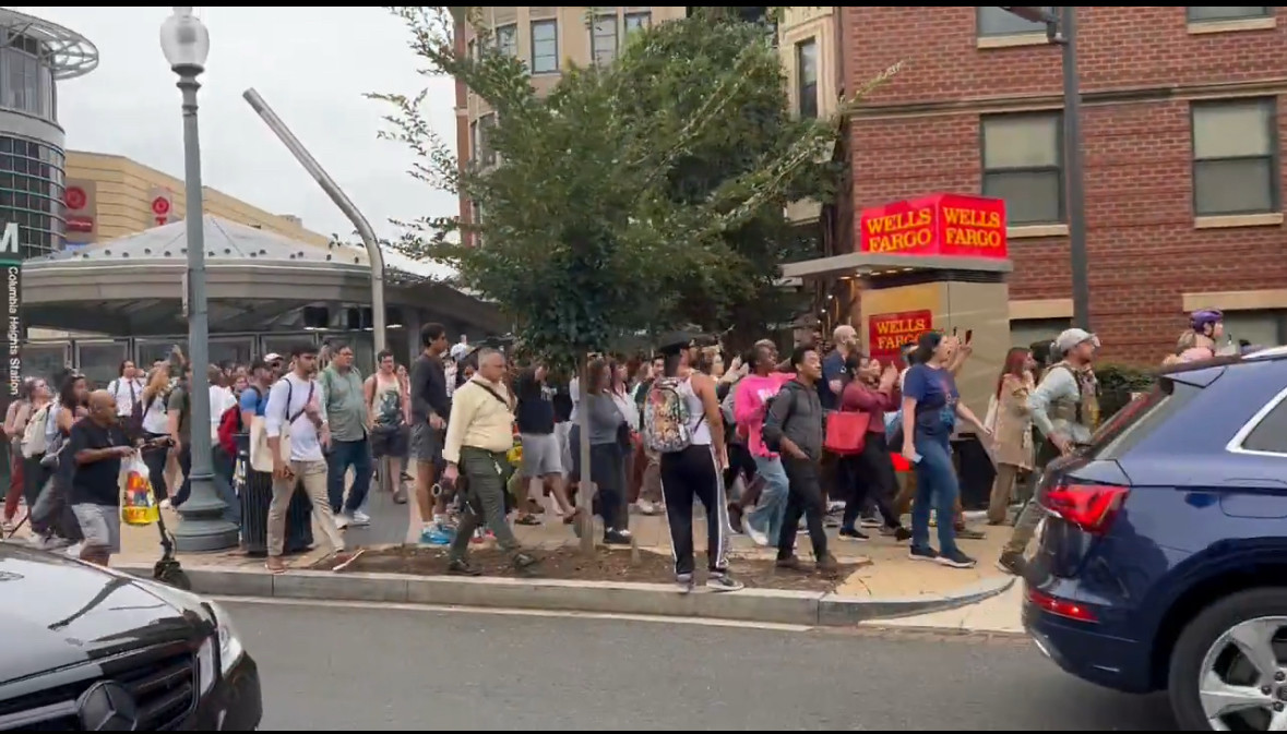 A screenshot of the video. A crowd of easily 50-70 people is amassed on the sidewalk yelling and chanting at ICE agents. There are white people, black people, Latinos, and Asians visible. There are and men and women (and maybe even some Enbies and trans folks, who knows), and a wide mix of ages from young 20-somethings to people who look in their 50s.