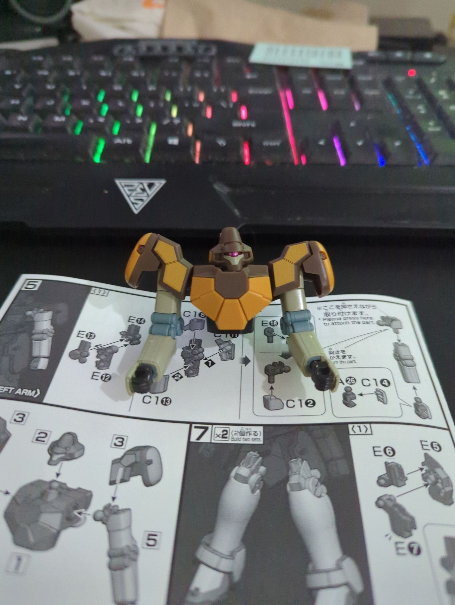 One half of the HGAC Maganac gunpla kit is completed, resting on its arms on the instruction booklet in front of a lit keyboard that frankly, could use a good clean