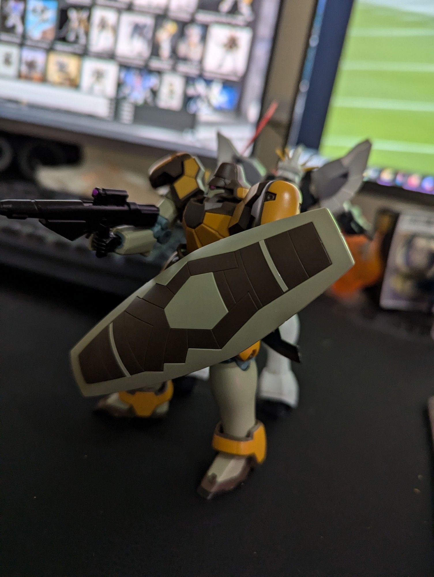 A completed HGAC Maganac gunpla hunched behind it's shield and aiming off camera with the Sandrock at its back