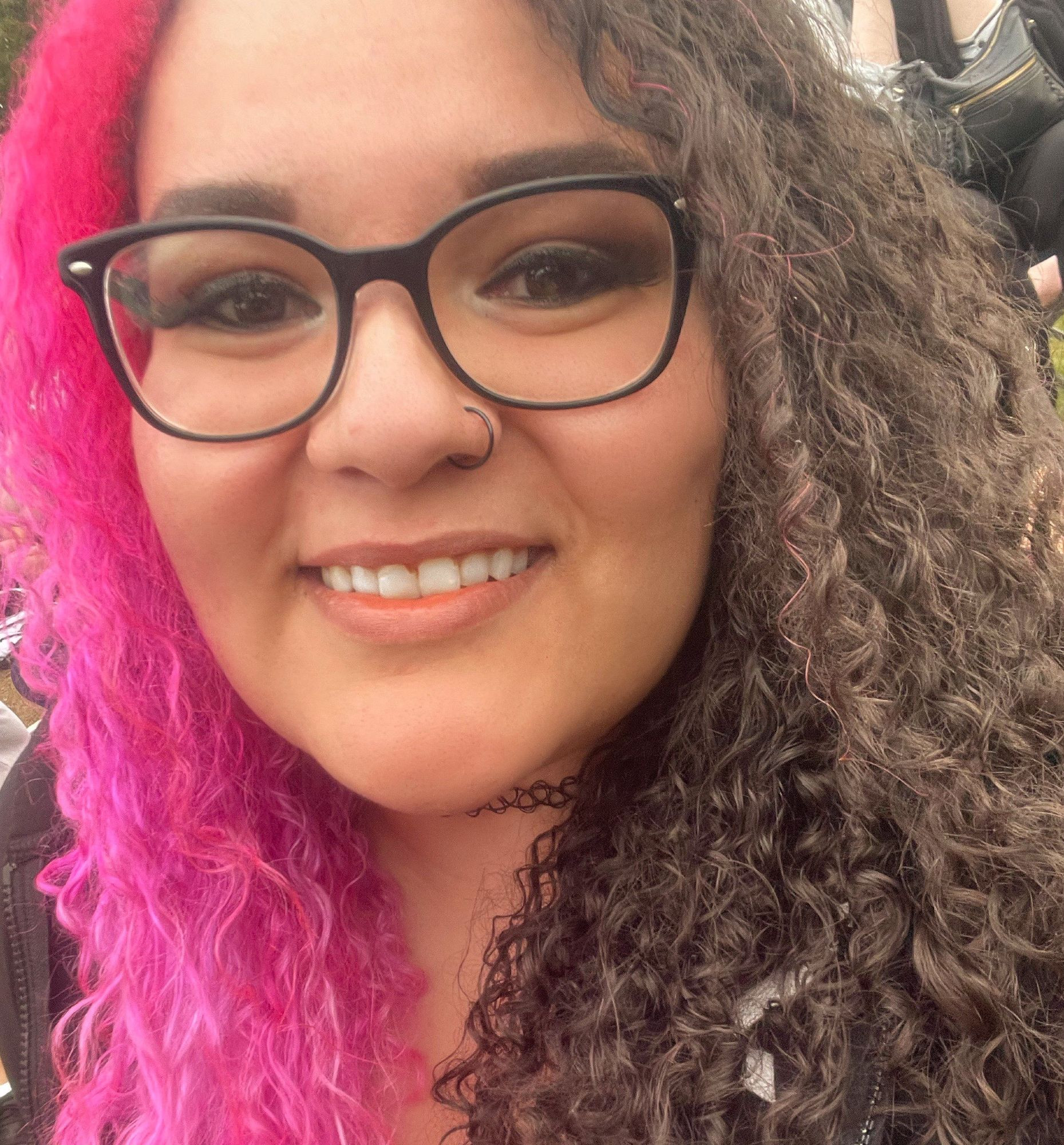 a selfie of a woman with curly dark brown hair with a pink split dye