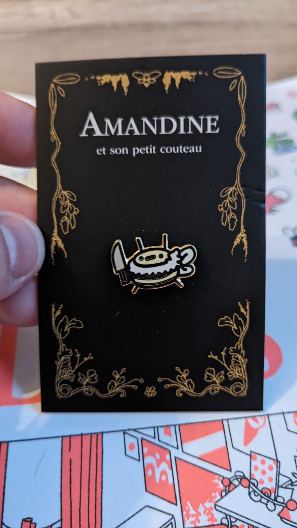 Un pins représentant une petite abeille qui tient un couteau. L'abeille s'appelle Amandine