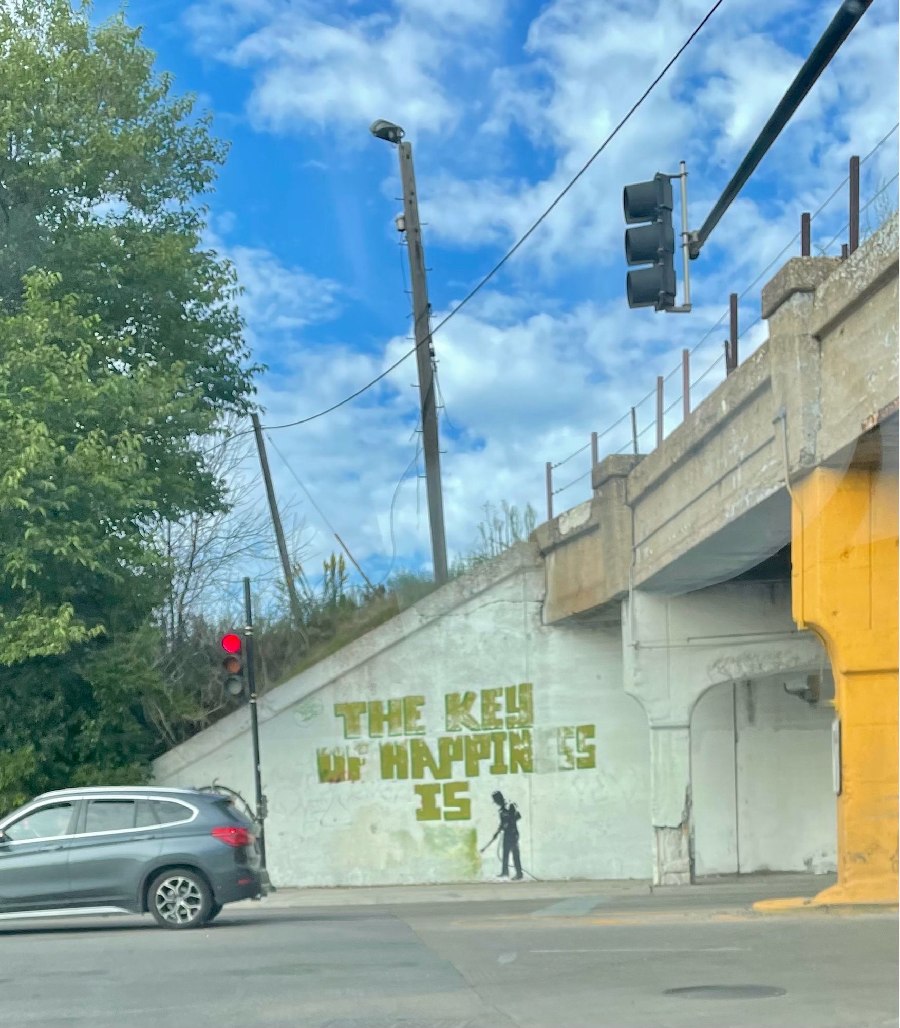 A graffiti that says “the key to happiness is “ and the last word is being power washed away by a painted man.