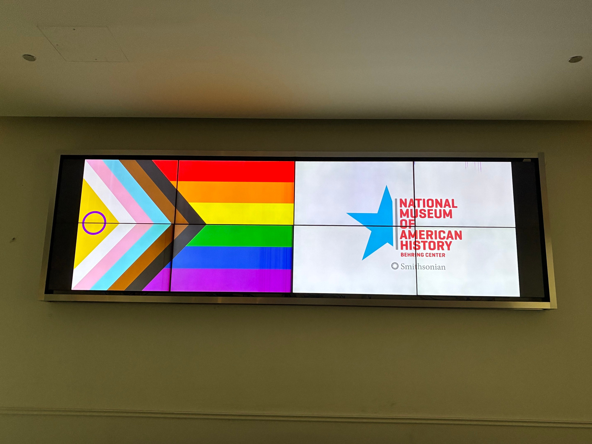 Video screen display with the LGBTQ Pride flag and sign showing “National Museum of American History”, a Smithsonian Museum in DC