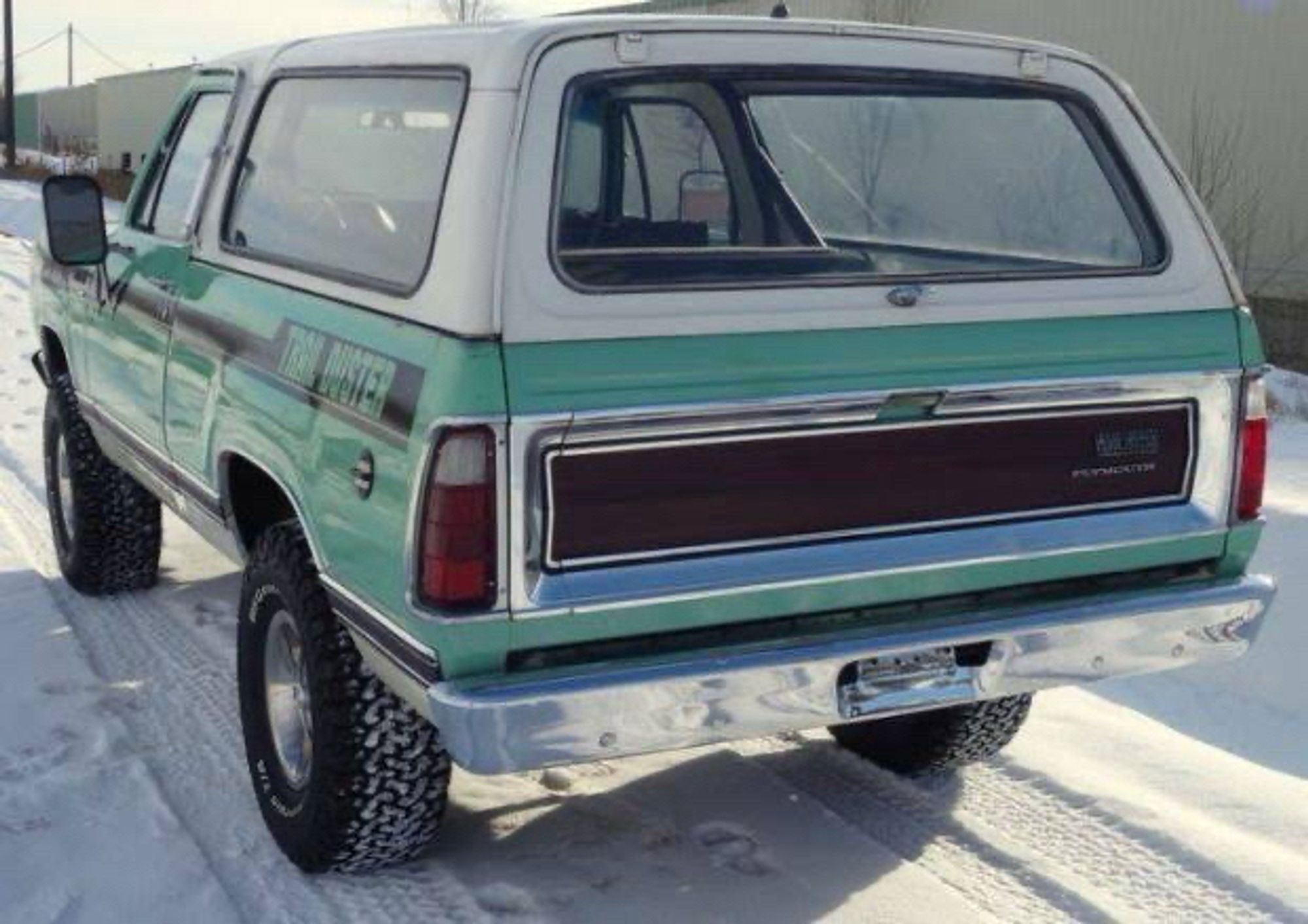 picture of rear of a mid 70s plymouth trailduster in the snow. it’s minty green and white with black graphics