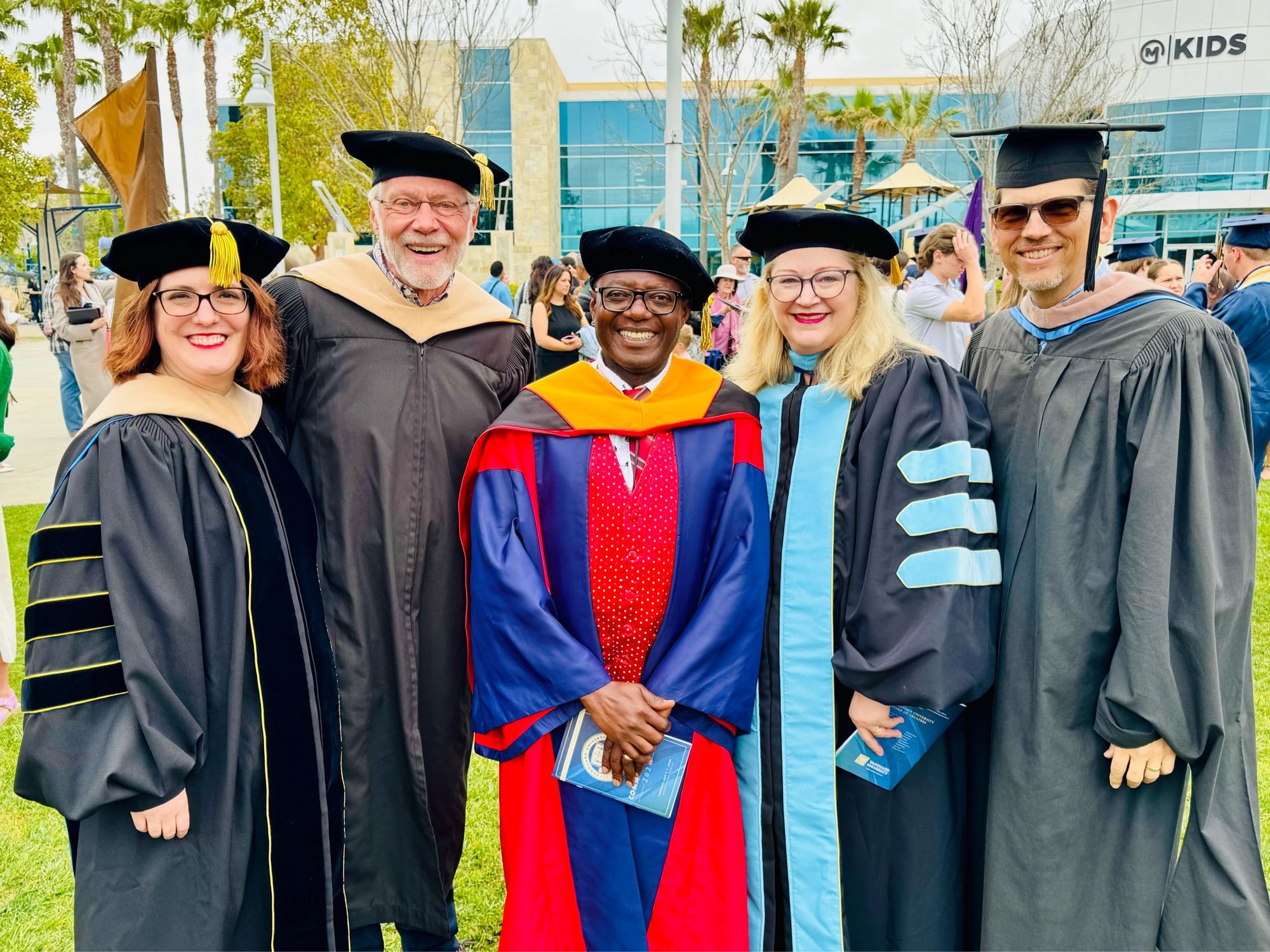 Five faculty wearing regalia smile at the camera