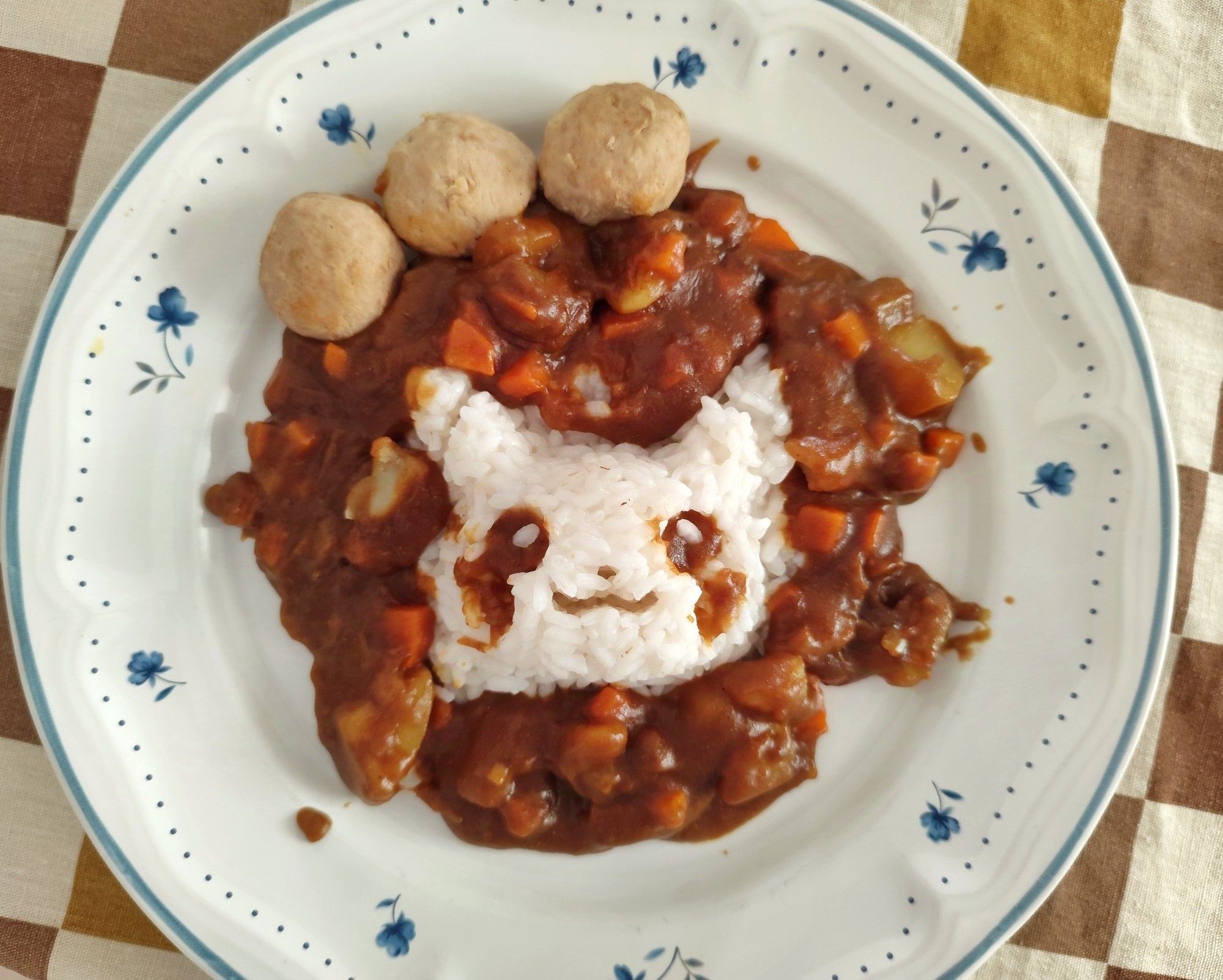 Photo of a plate with a Pikachu-shaped serving of rice surrounded by Japanese curry and adorned with three meatballs.