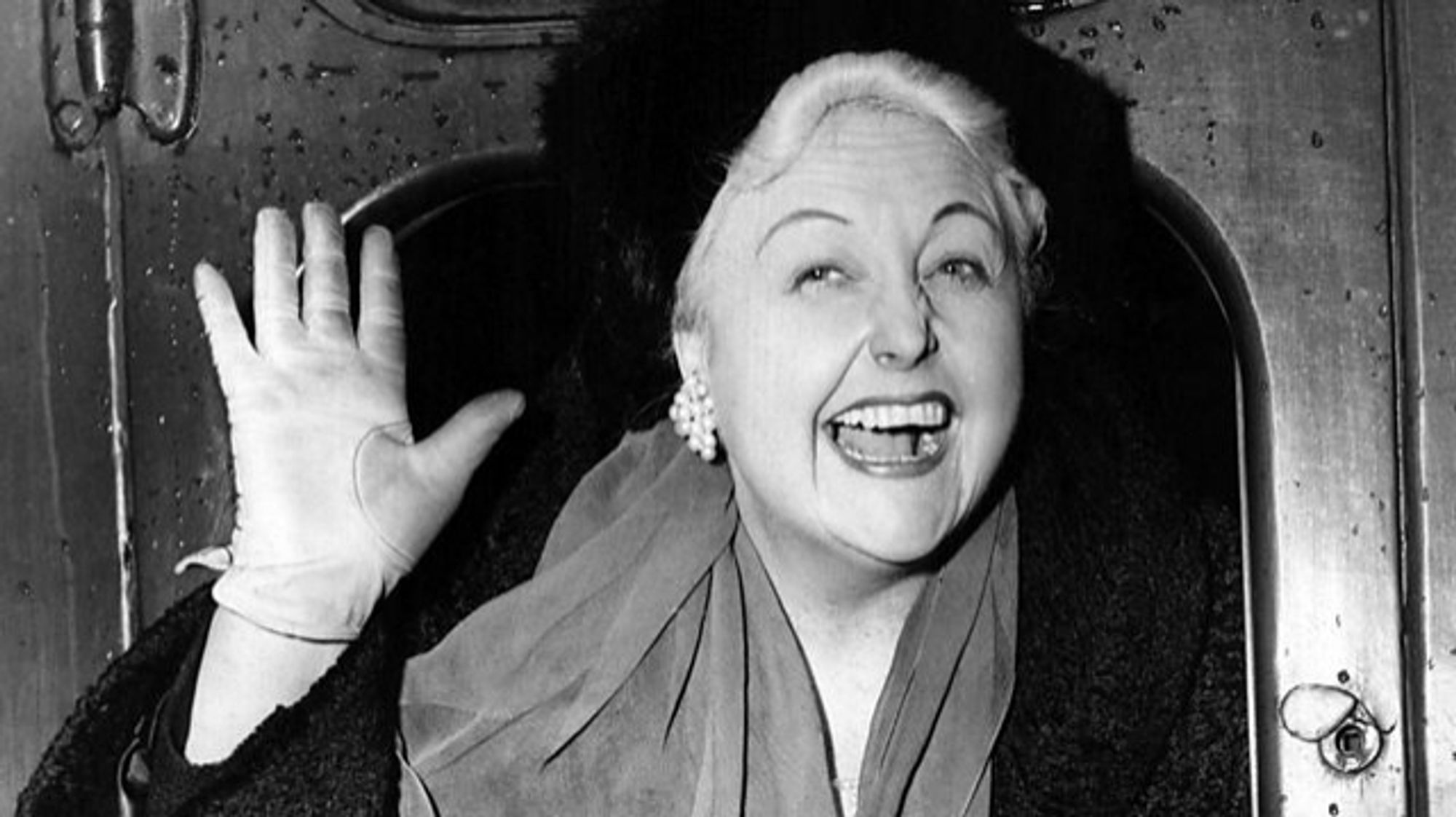 Welsh comedianne and banjo player Tessie O'Shea waving from an open train window c.1955