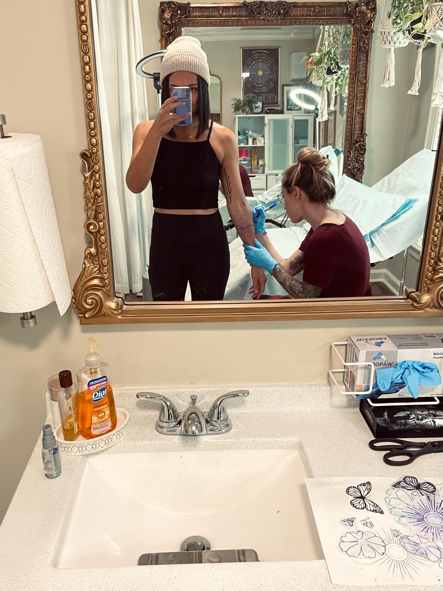 Mirror selfie of poster standing while tattoo artist draws on part of tattoo stencil 