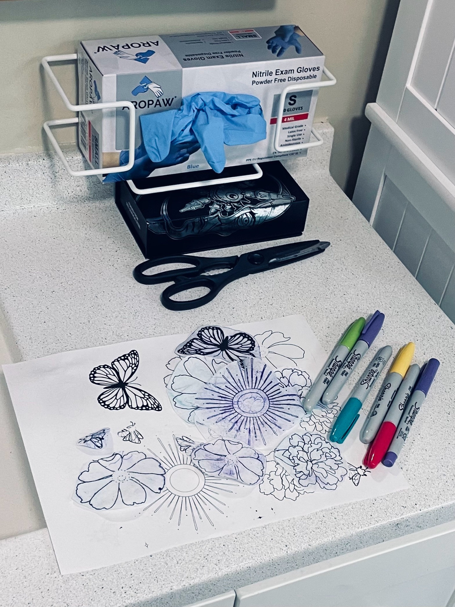 Traditional tattoo stencils and a variety of different colored sharpies on a counter 