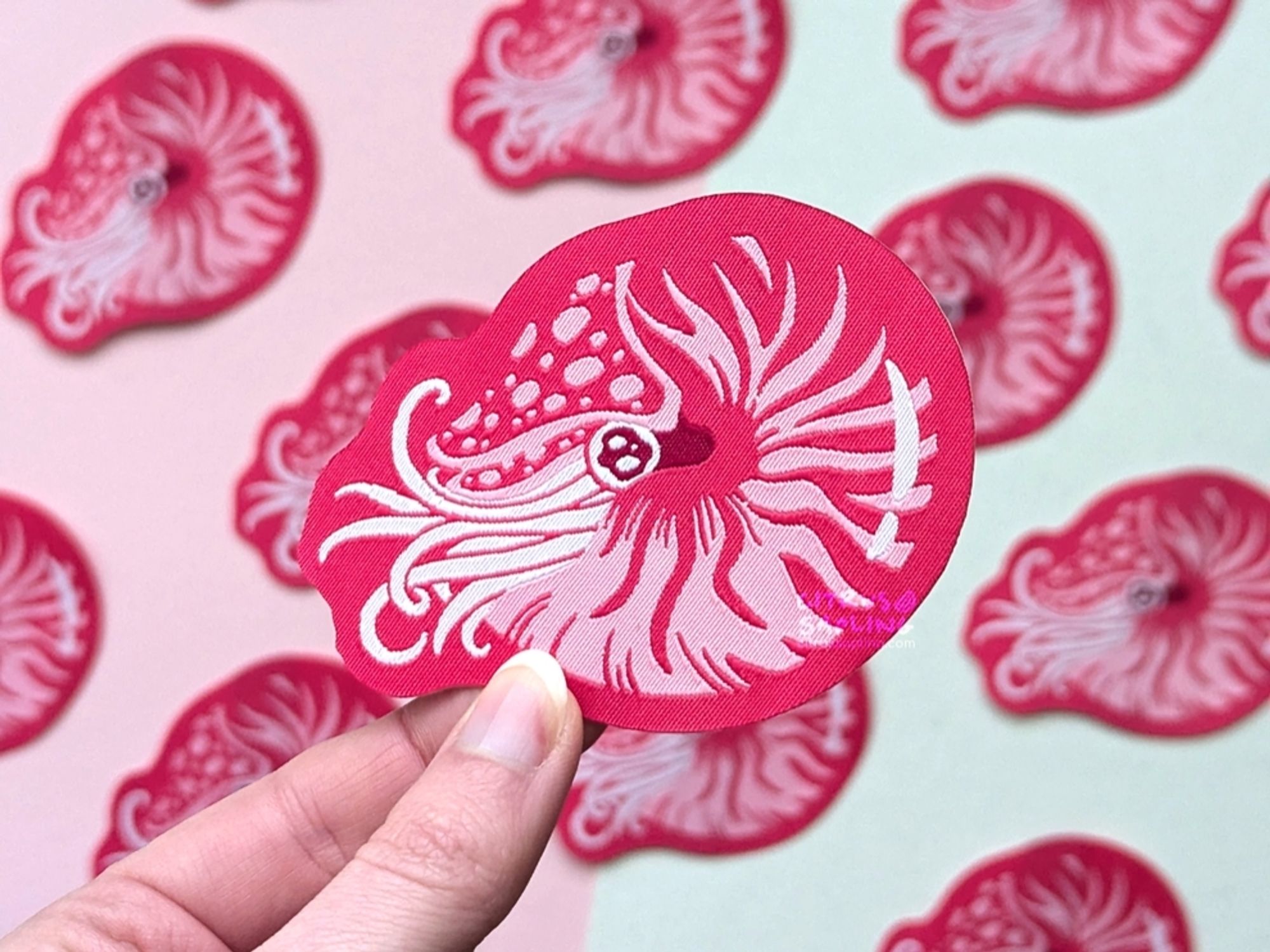 A woven patch featuring a nautilus in reds and pinks, with more of them in the background