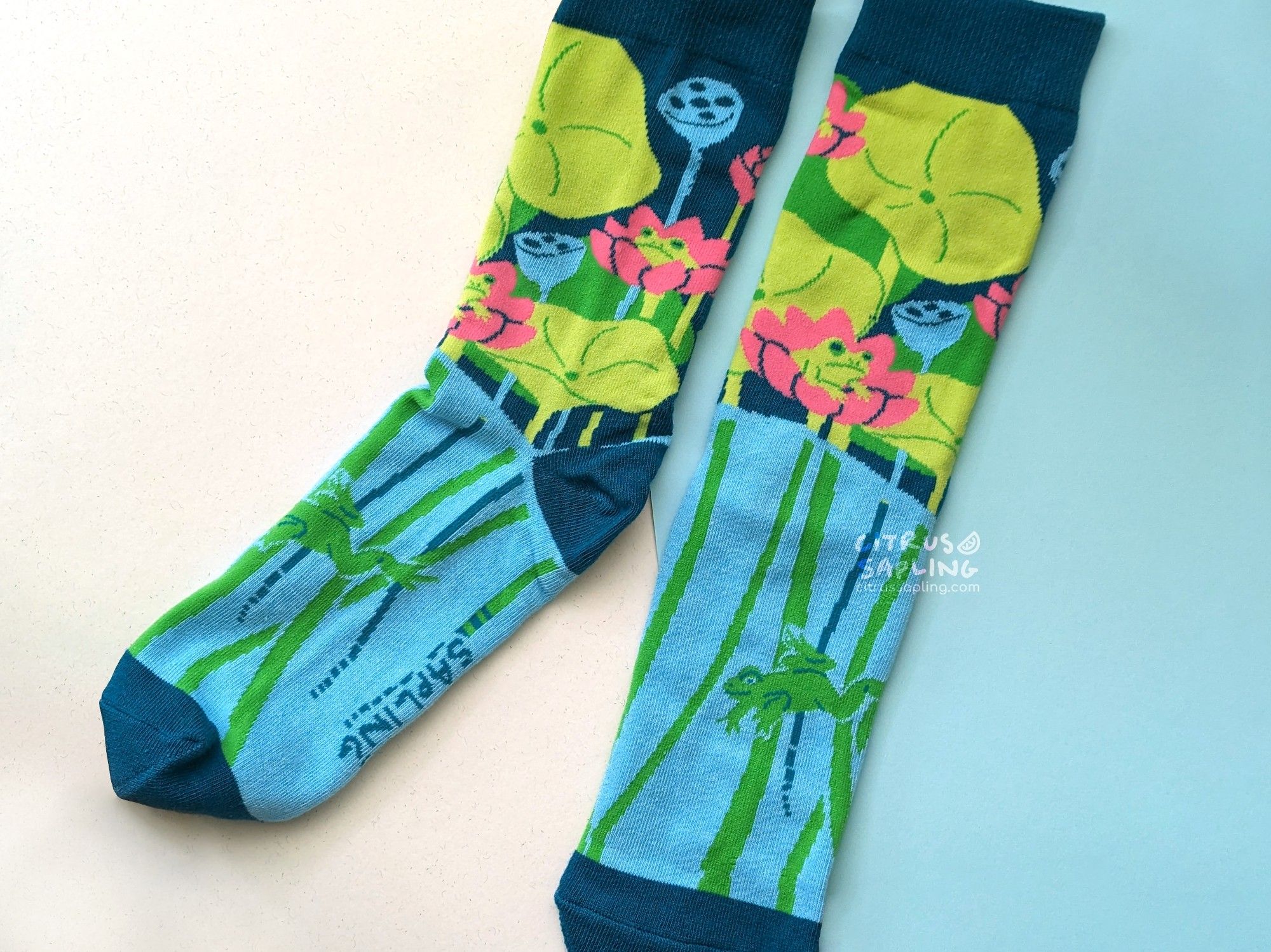 Socks with lotus leaves and flowers, with frogs sitting in the flowers. The stems extend below the water on the bottom half of the sock, where there is another frog swimming