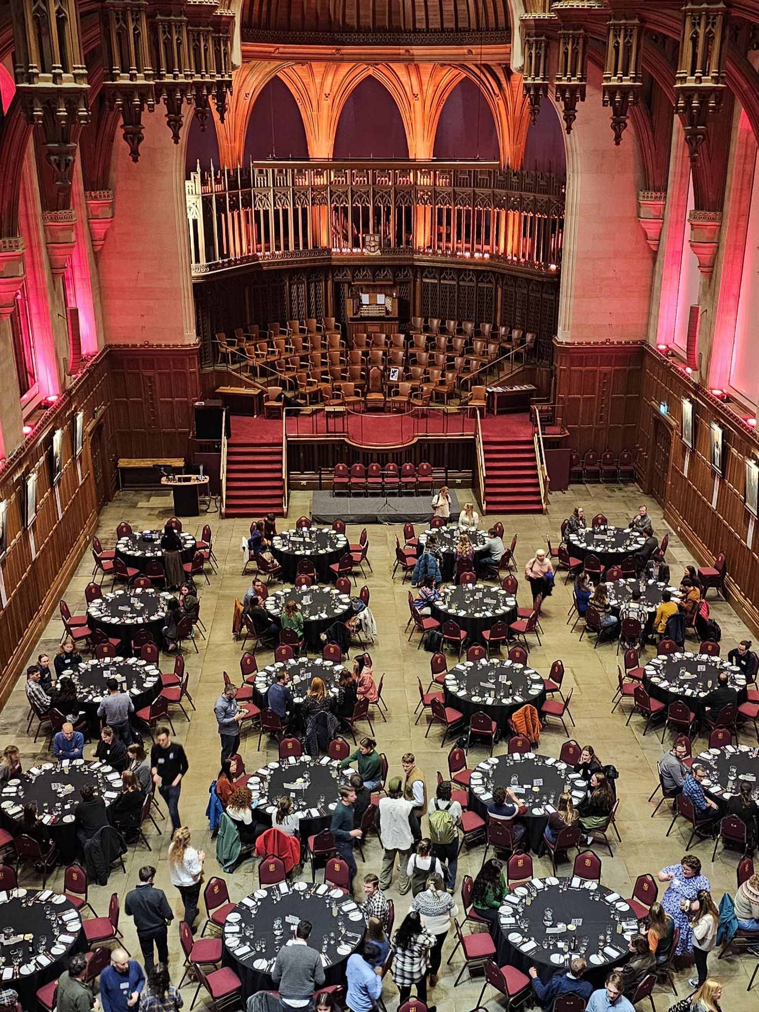 Photo looking down on the conference dinner. People are sat round circular tables in a grand hall with a vaulted ceiling and a pipe organ.