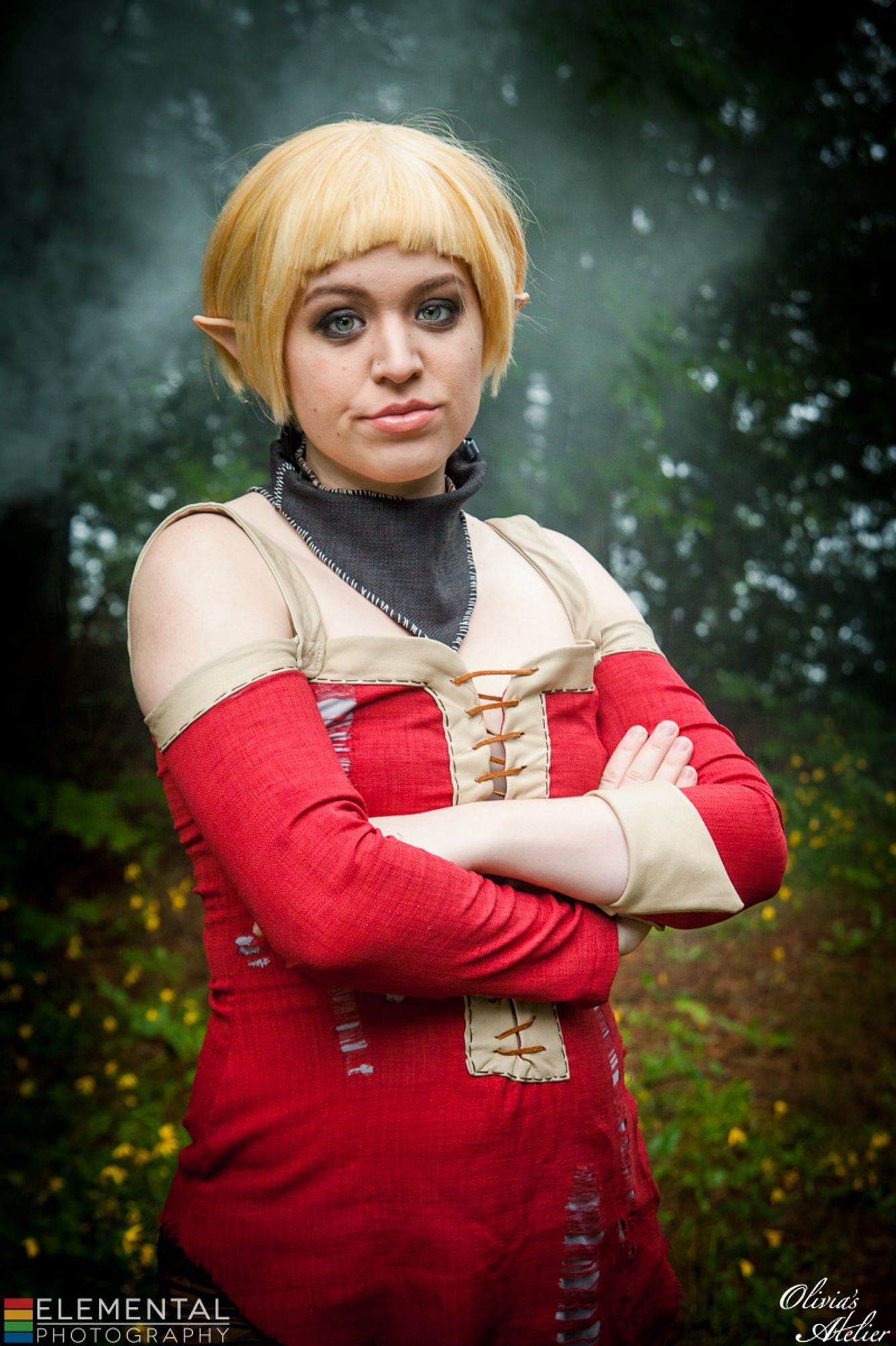 A white non-binary person dressed as Sera from Dragon Age: Inquisition. They are looking at the camera with a disappointed face and their arms are crossed.