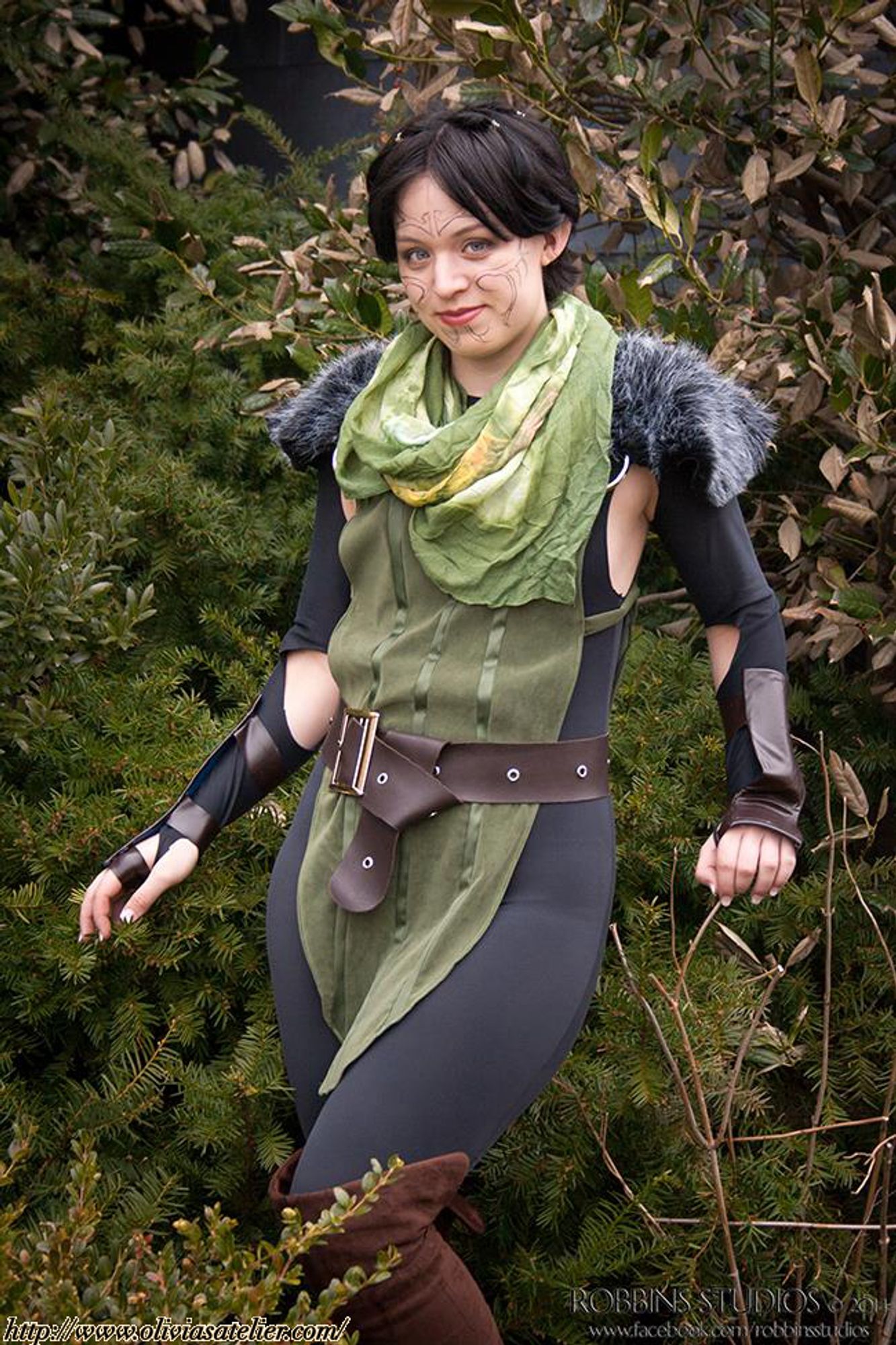 A white, non-binary person dressed as Merrill from Dragon Age 2. They are posed among some foliage like a dainty elf.