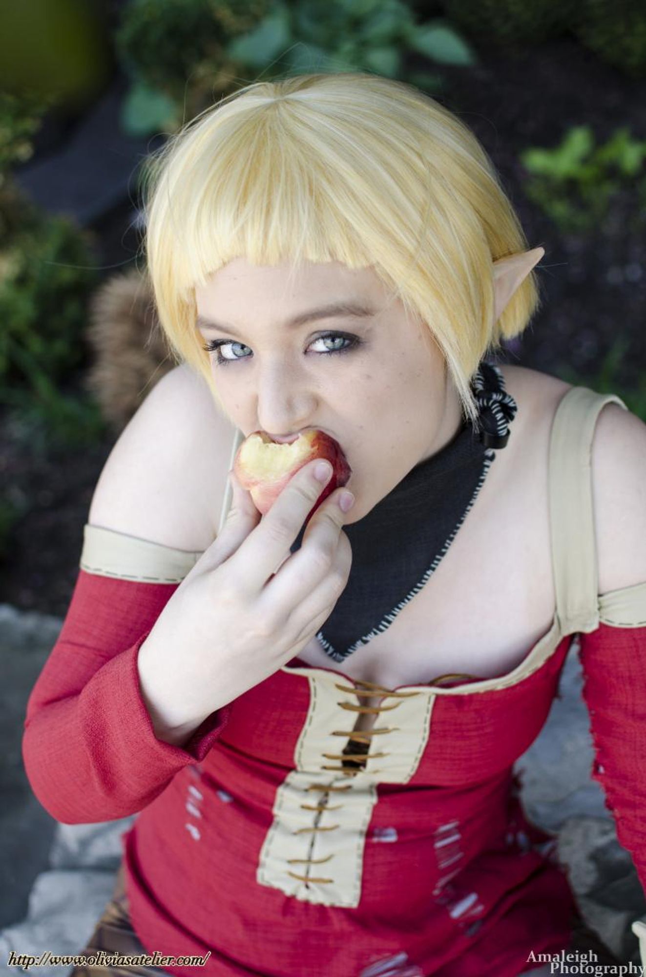 A white non-binary person dressed as Sera from Dragon Age: Inquisition. They are looking directly into the camera while they eat a peach.