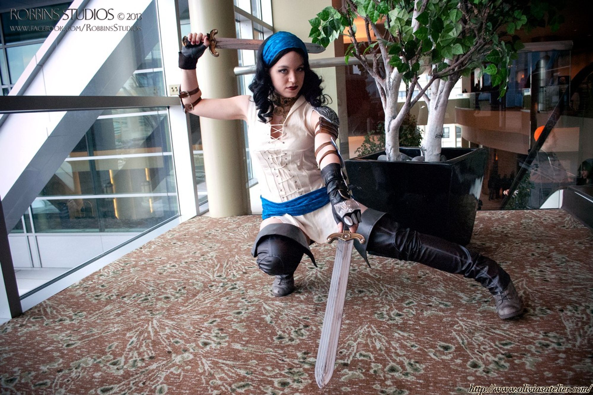 A white, non-binary person dressed as Isabela from Dragon Age 2. They are posed with one sword behind their head, and the other toward the camera with one of their legs splayed out to the side.