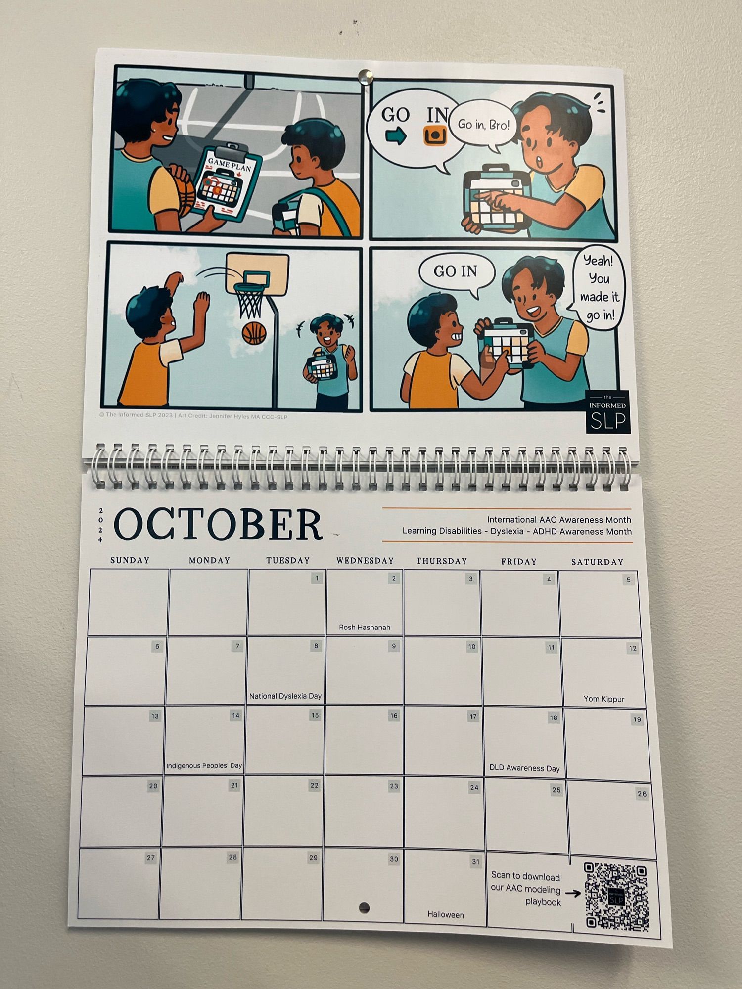 Wall calendar open to the month of October. There’s a cartoon with an AAC device being used to model “go in” while playing basketball. It also lists that October is International AAC awareness month, learning disabilities, dyslexia, & ADHD awareness month. And that Oct 18 is DLD awareness day.