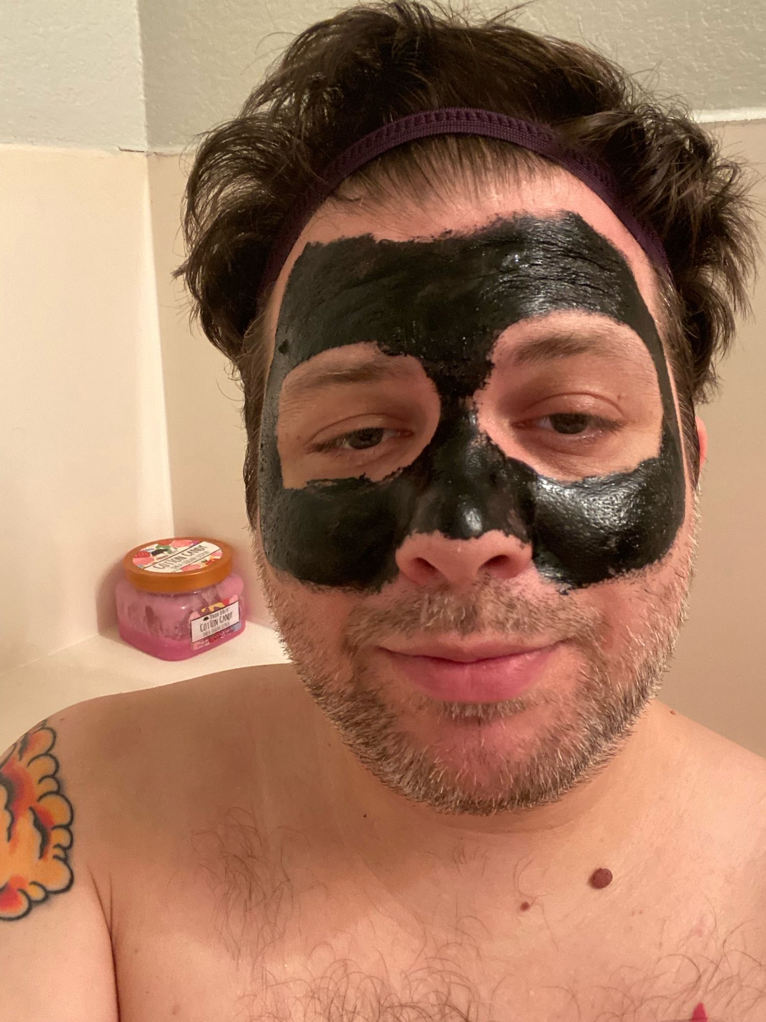 Very high man in bath tub with hair up and half his face in a black mask.